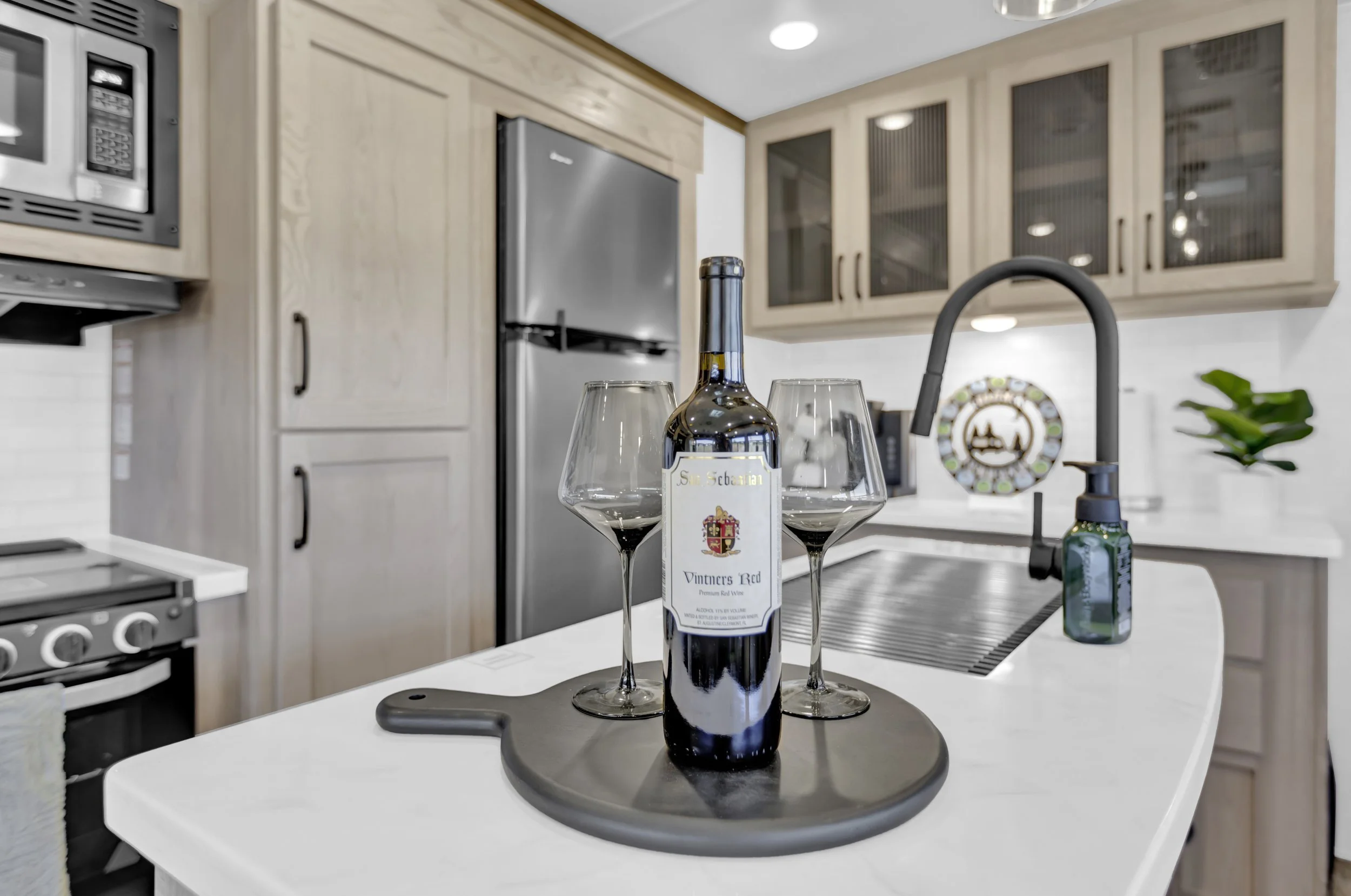A bottle of red wine and two empty wine glasses on a black tray in a modern kitchen.