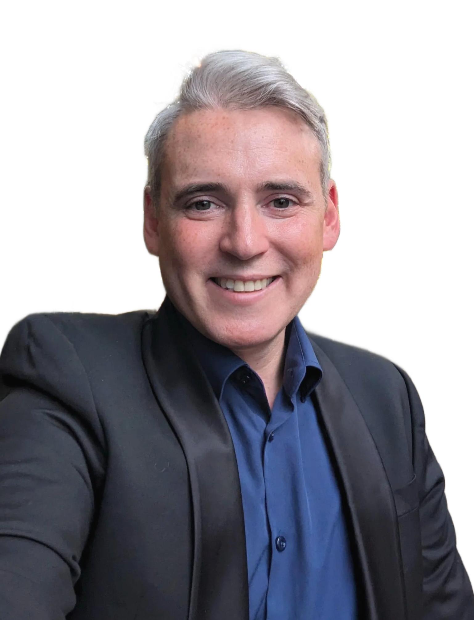 A smiling man with short gray hair, wearing a dark blazer over a blue shirt, taking a selfie.