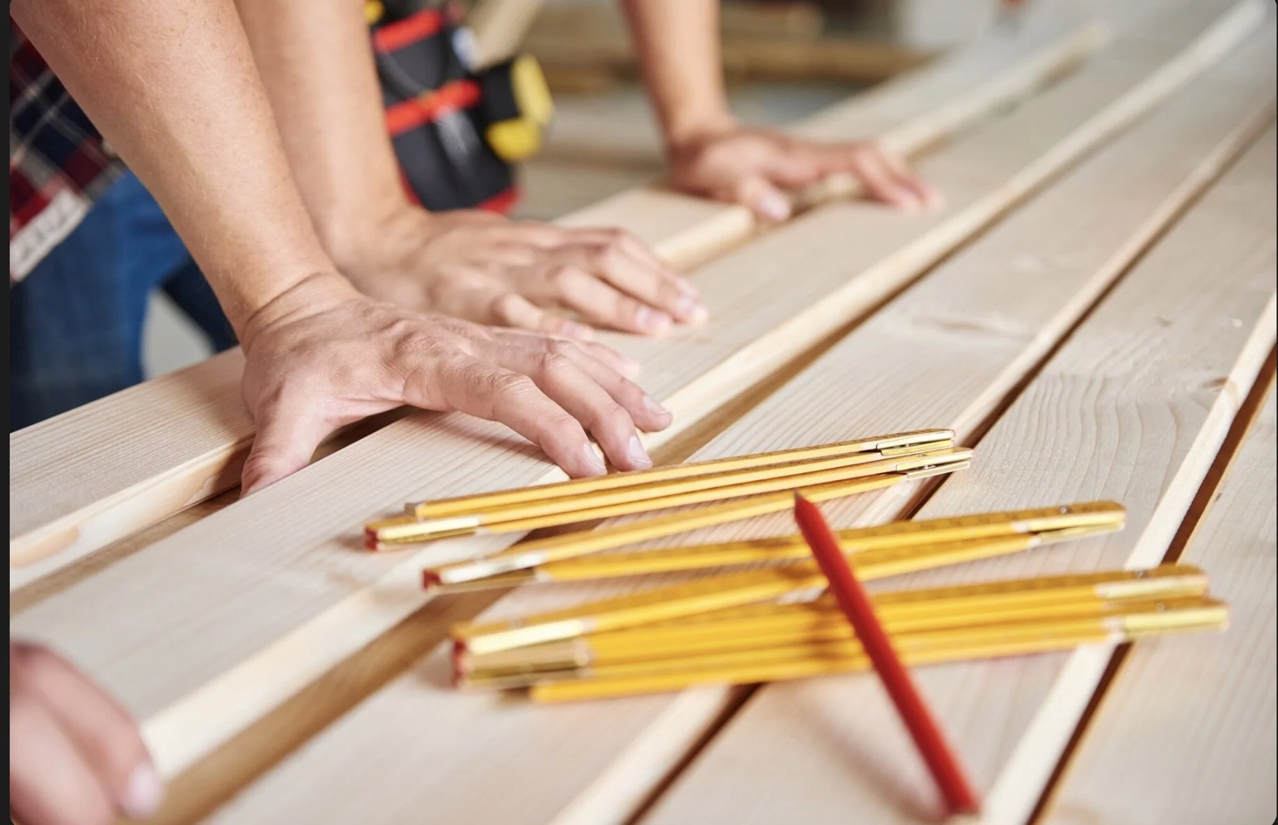 People working on a woodworking project, measuring and arranging wooden planks on a workbench.