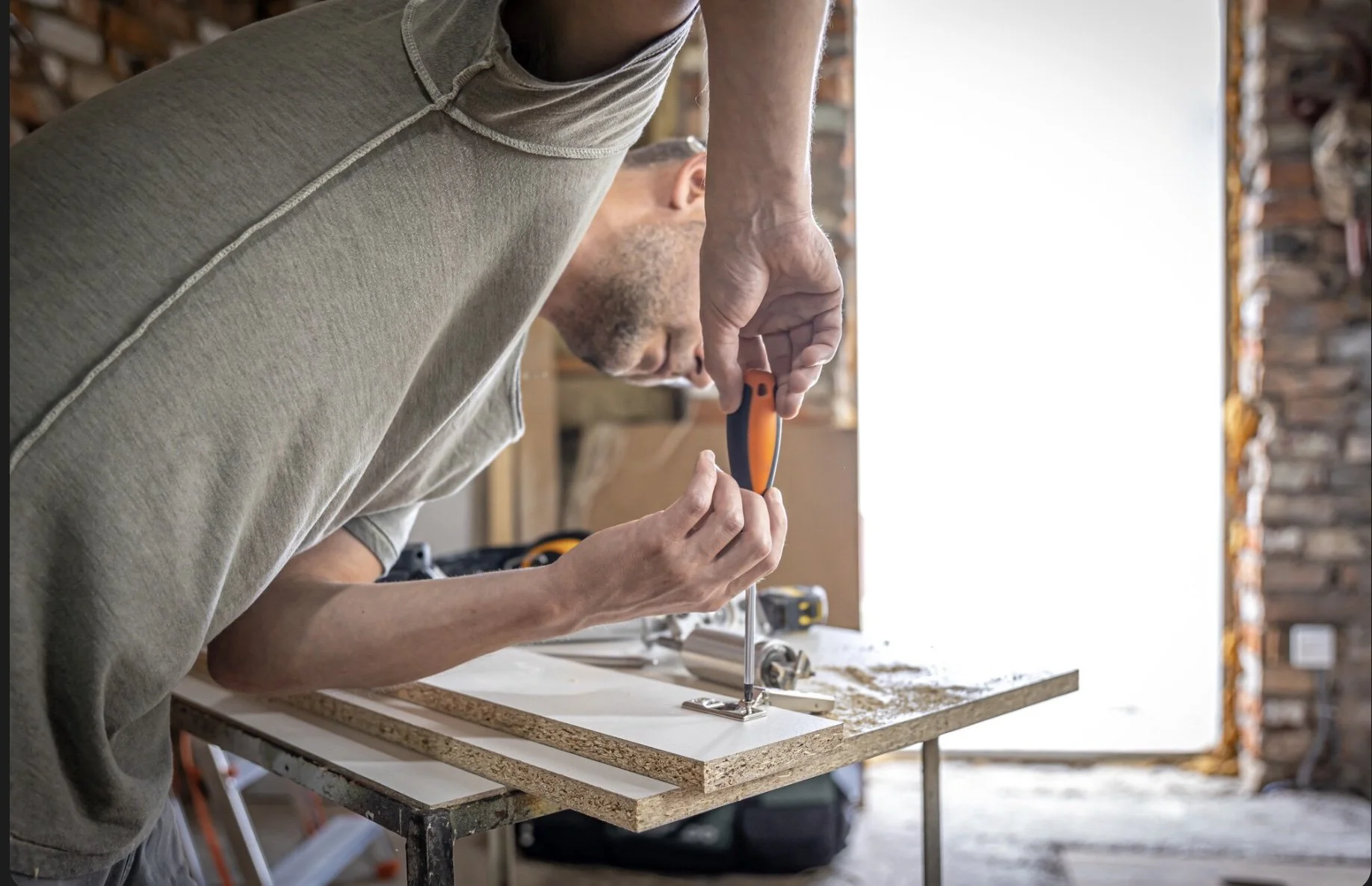 A man using a screwdriver to assemble a piece of furniture in a workshop.