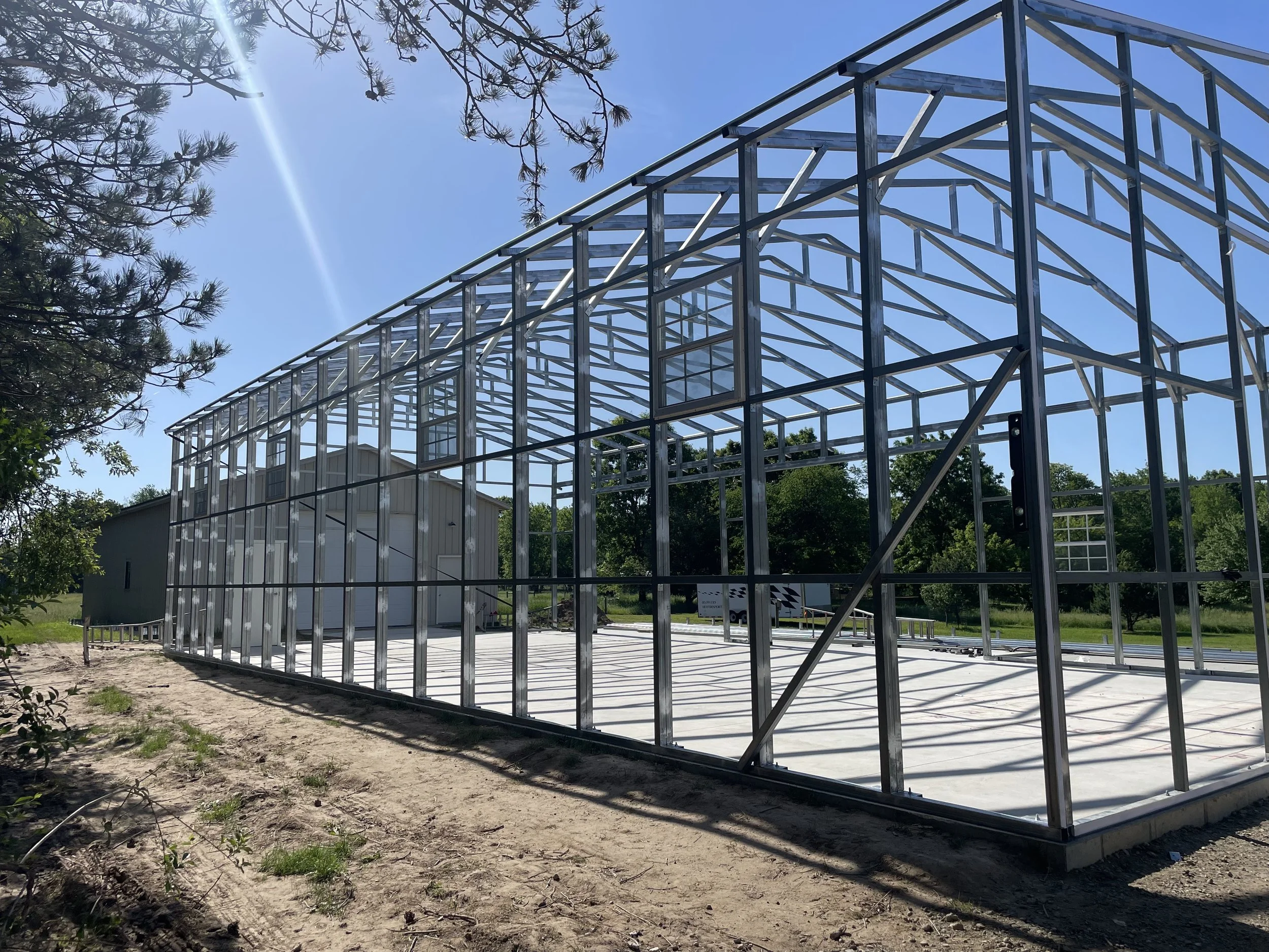 A metal framework of a building under construction with a clear blue sky and trees in the background.