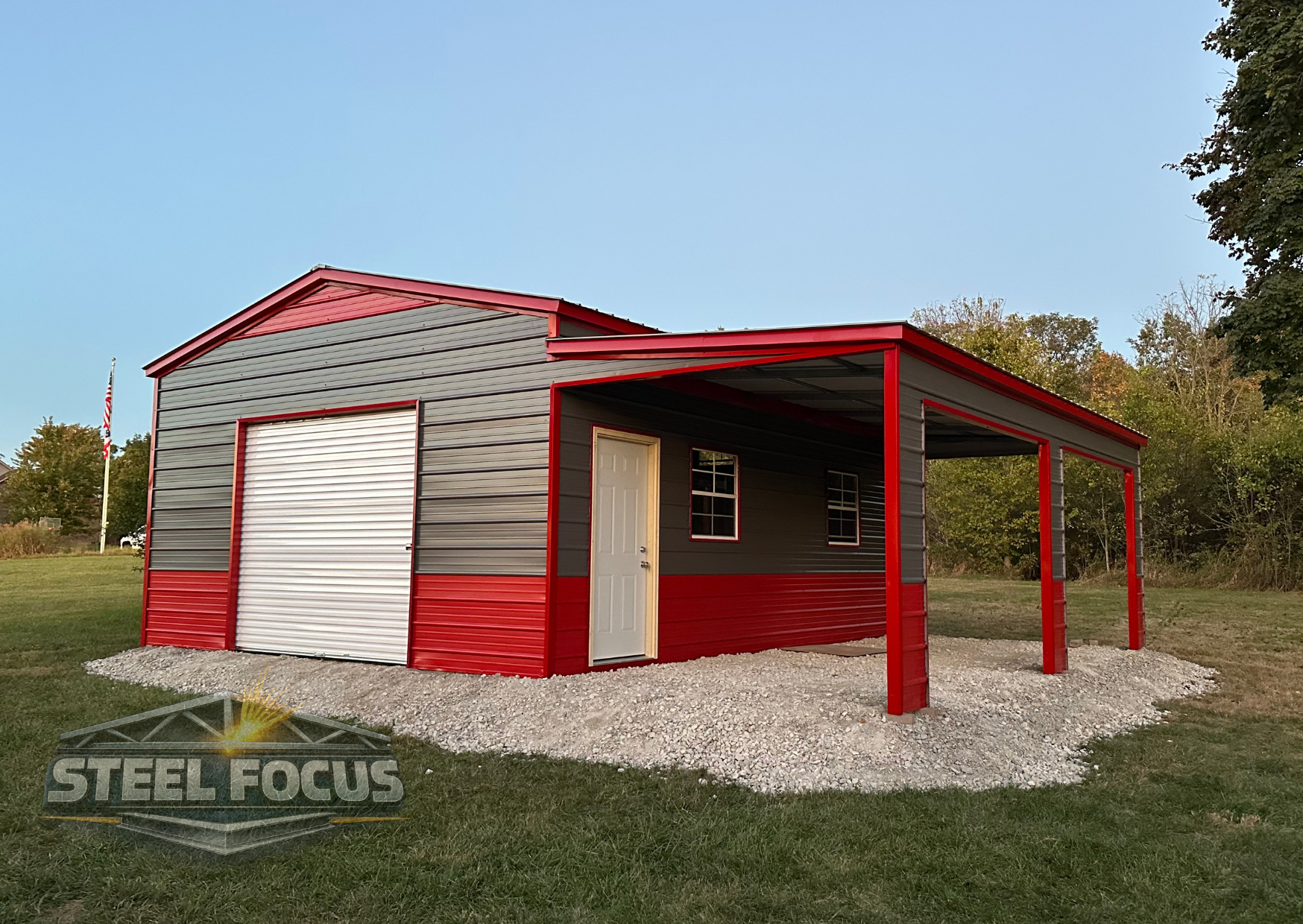 Gray and red metal storage shed with a large roll-up door, a side door, and two small windows, situated on a gravel foundation in a grassy area with trees in the background.