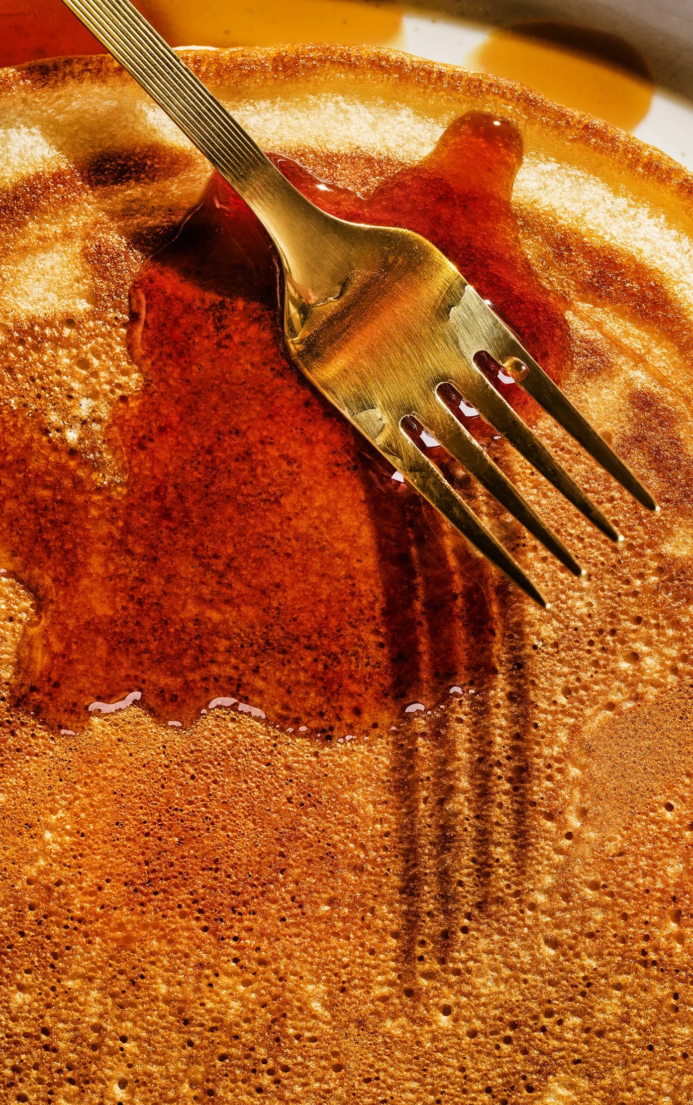 Close-up of a fork stabbing a frothy, golden-brown pancake with syrup.