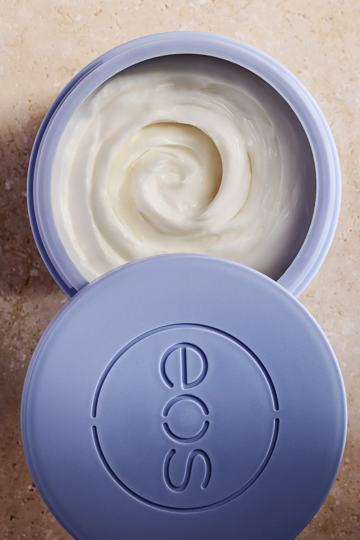 A lotion product in purple container against a pink stone surface. Product beauty photography by Nutmeg Imageworks.