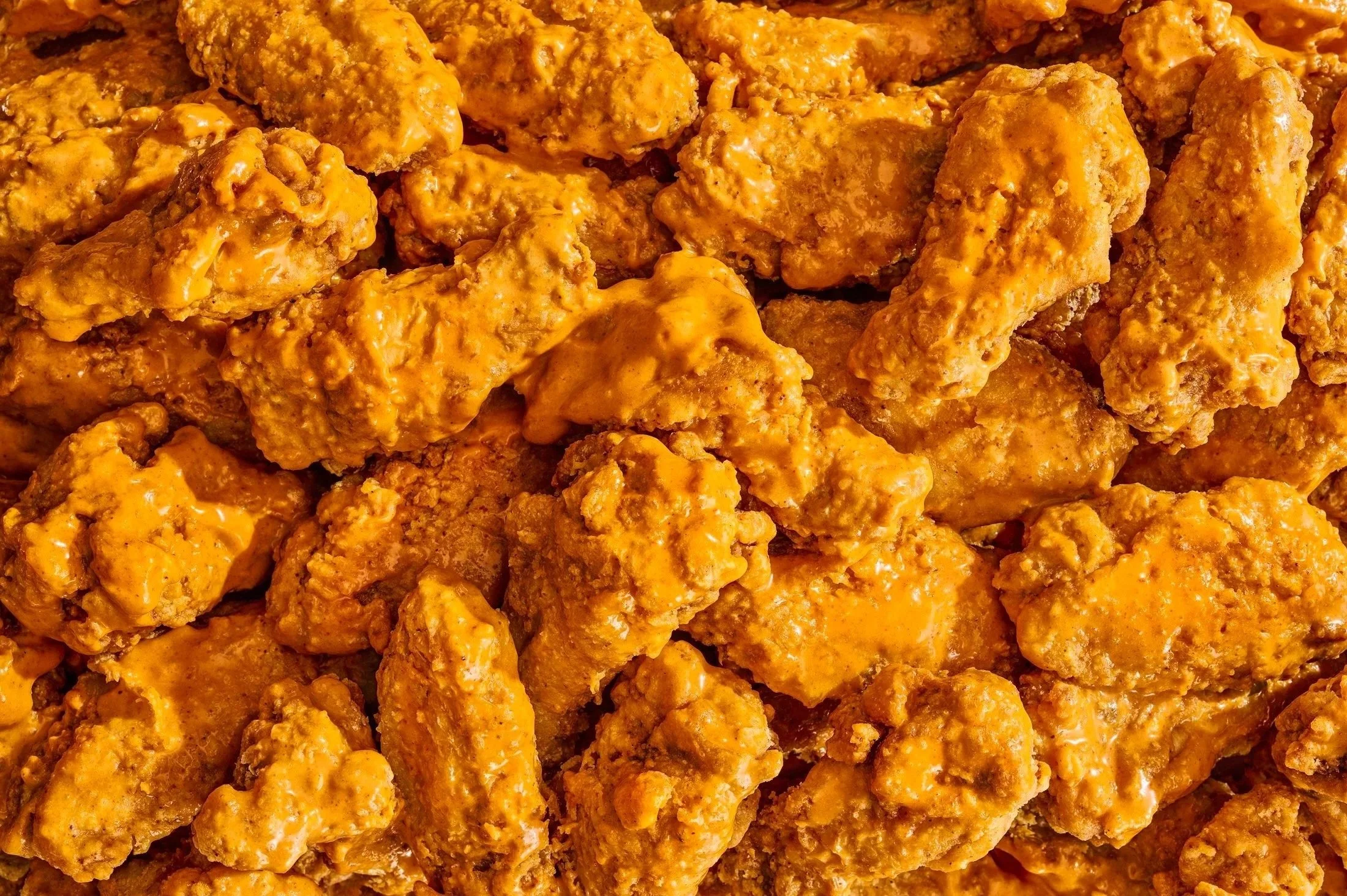 Close-up of fried chicken pieces coated in orange-colored sauce.