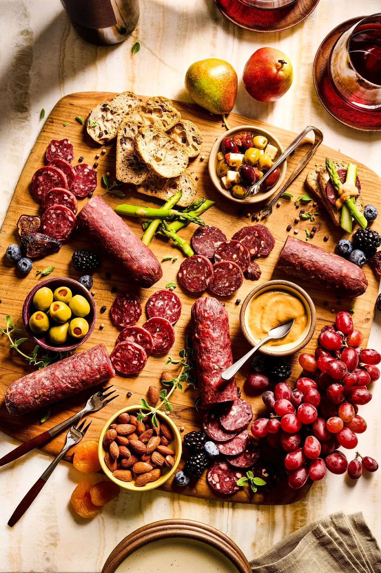 A wooden charcuterie board with an assortment of cured meats, cheeses, berries, olives, nuts, bread slices, and a small bowl of mustard or dipping sauce.