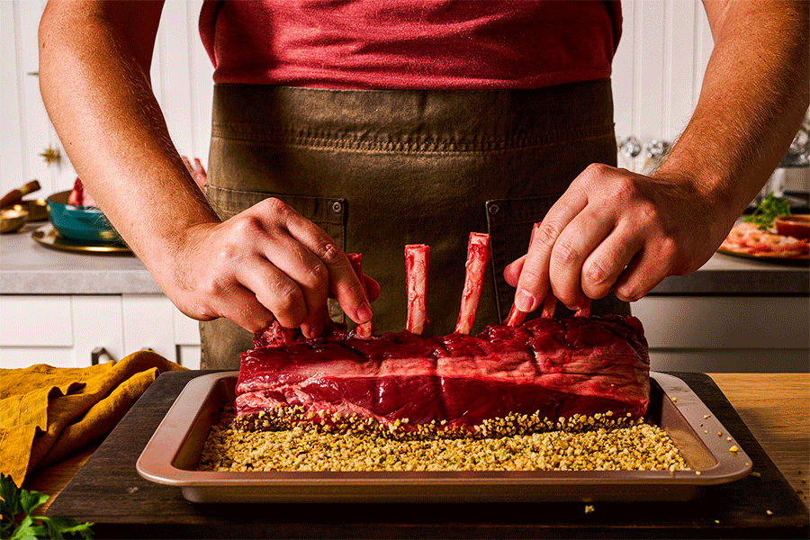Person preparing a raw rack of beef ribs on a tray with yellow seasoning, in a kitchen.
