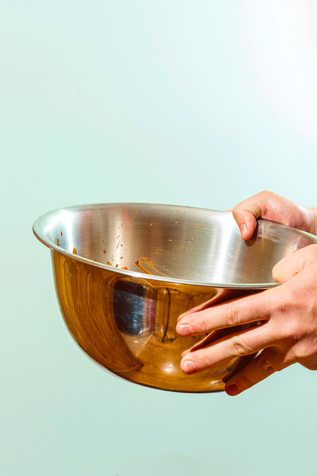 Person holding a metal mixing bowl with some leftover batter inside. Food photography gif.