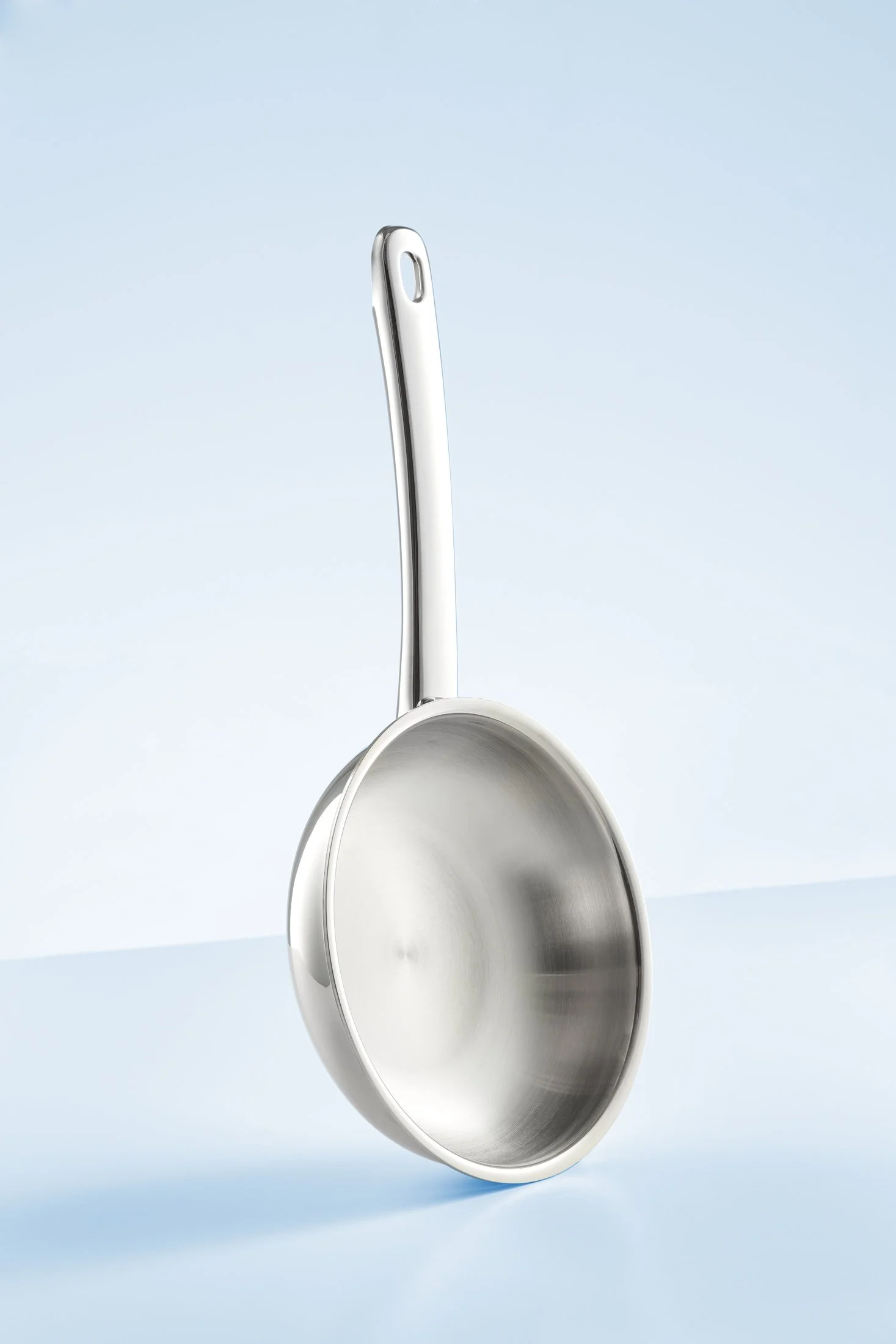 A stainless steel ladle hanging upside down against a light blue background.