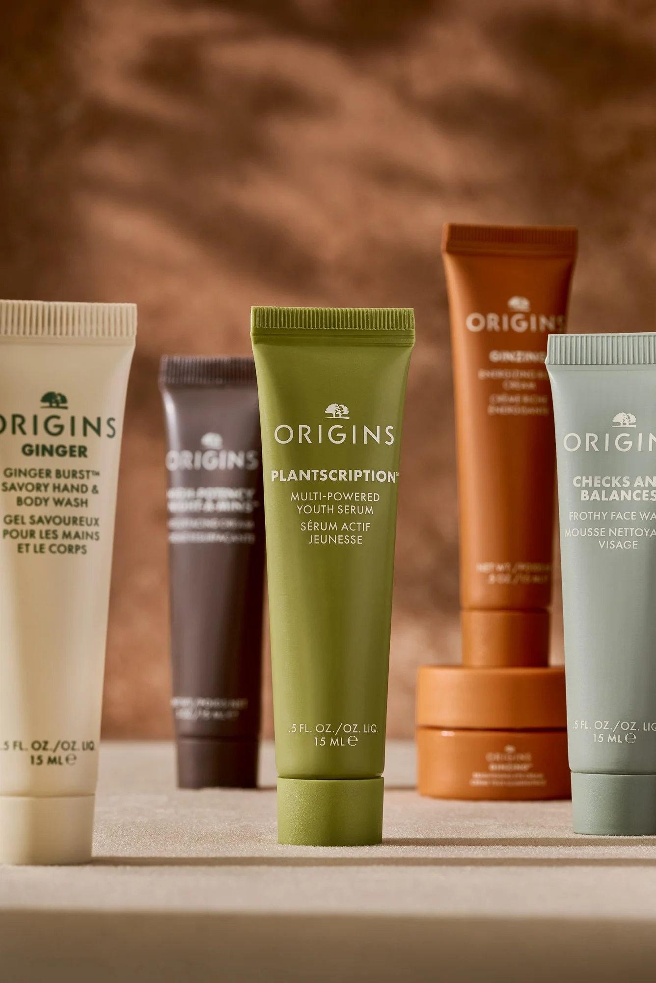Various origins skincare product tubes with colorful packaging on a neutral surface, copper background with shadows. Product beauty photography by Nutmeg Imageworks.