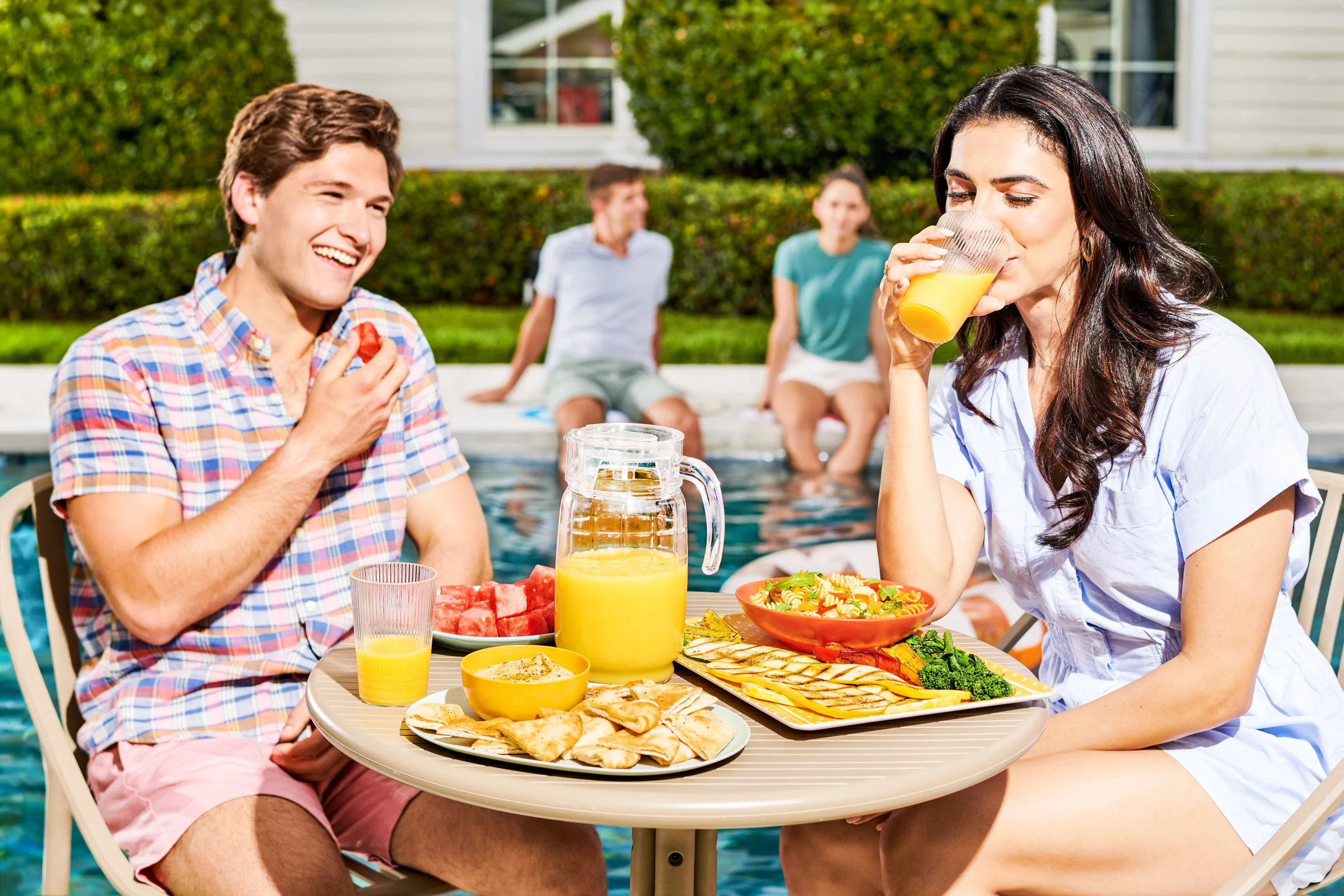 Lifestyle photography of a woman and man enjoying a poolside meal with friends on a sunny day.