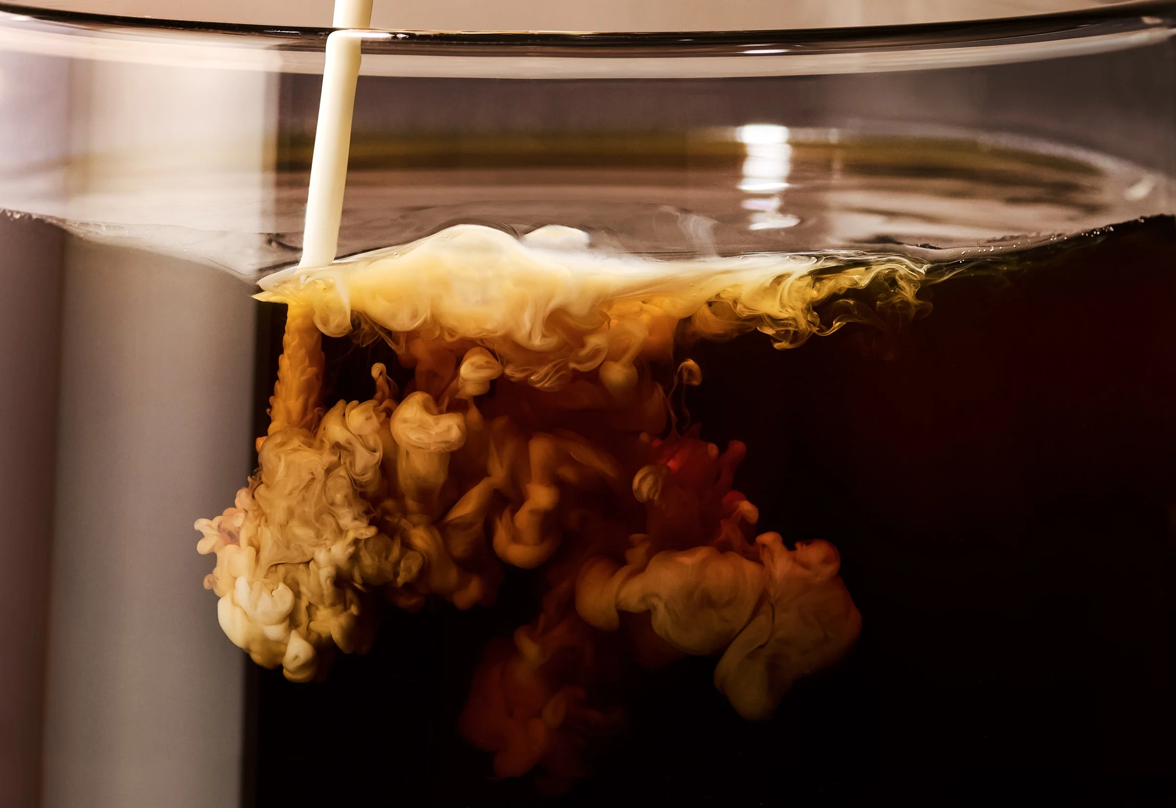 Cream or yellow dye being poured into dark water, creating a swirl of colors.