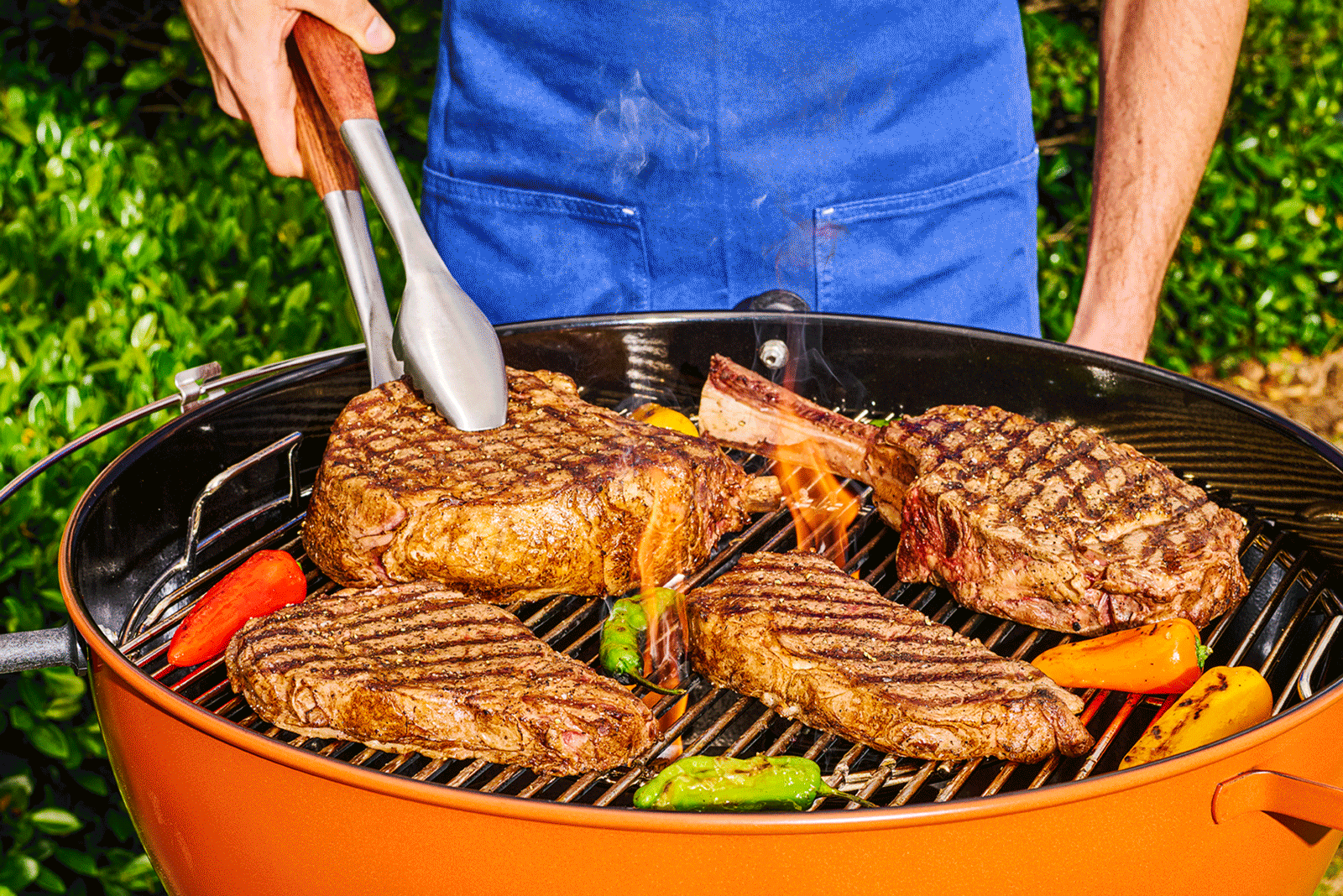 Person cooking steaks and peppers on an outdoor grill.