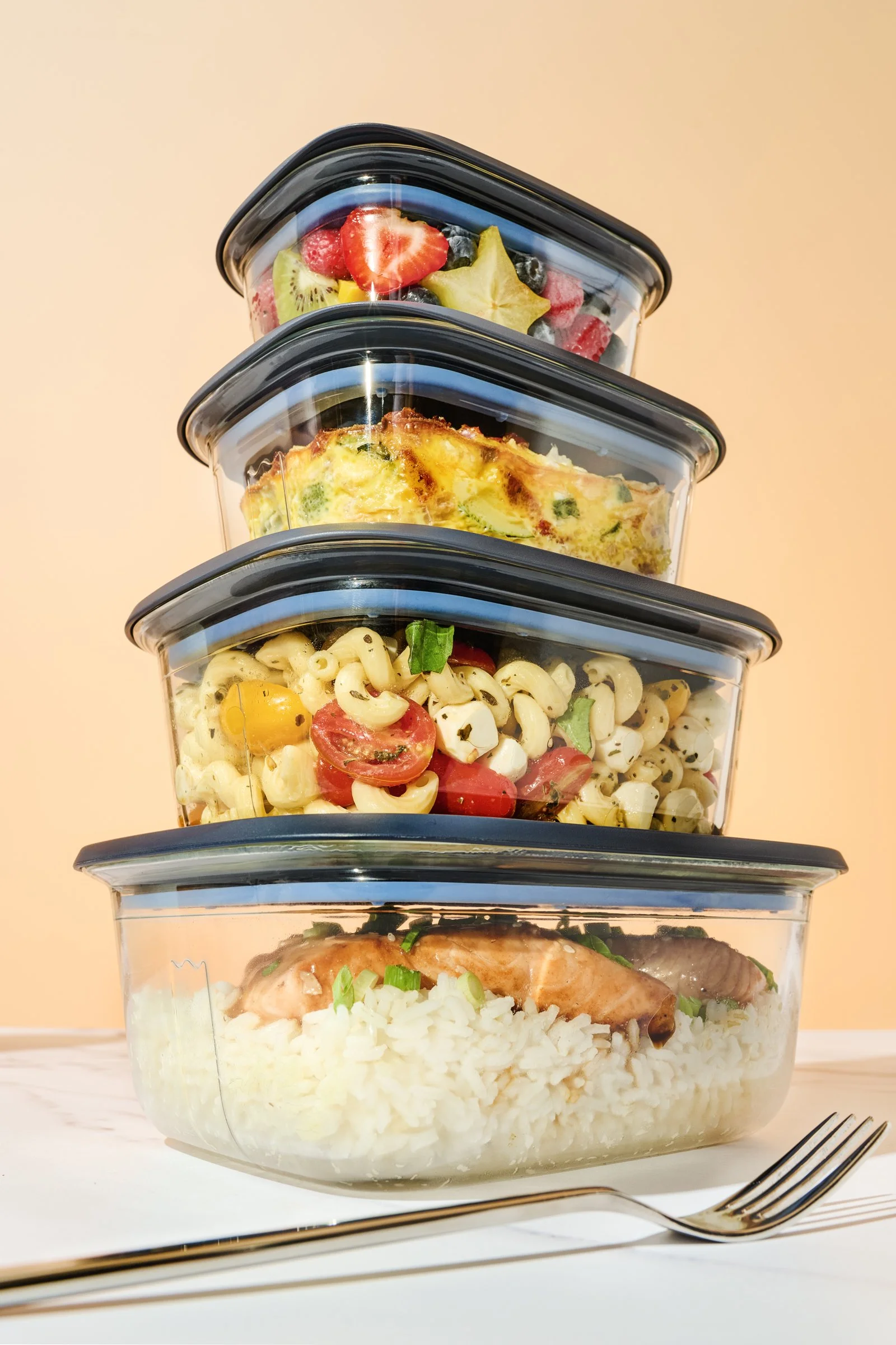 Product photography of stacked glass containers with styled meals inside from a low dramatic angle.