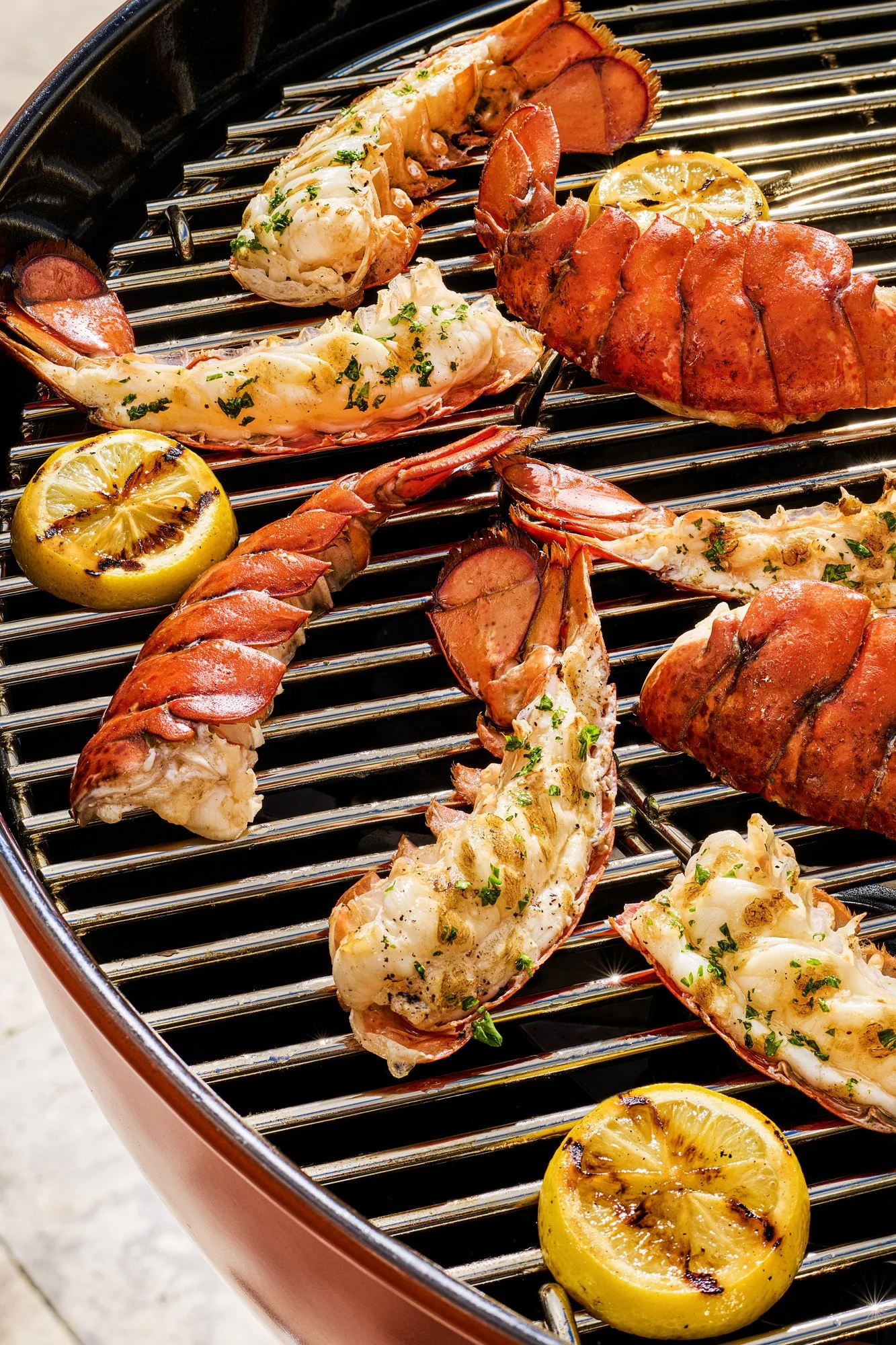 Lobster tail halves, large lobster claw, grilled lemon halves, and grilled shrimp on a barbecue grill.