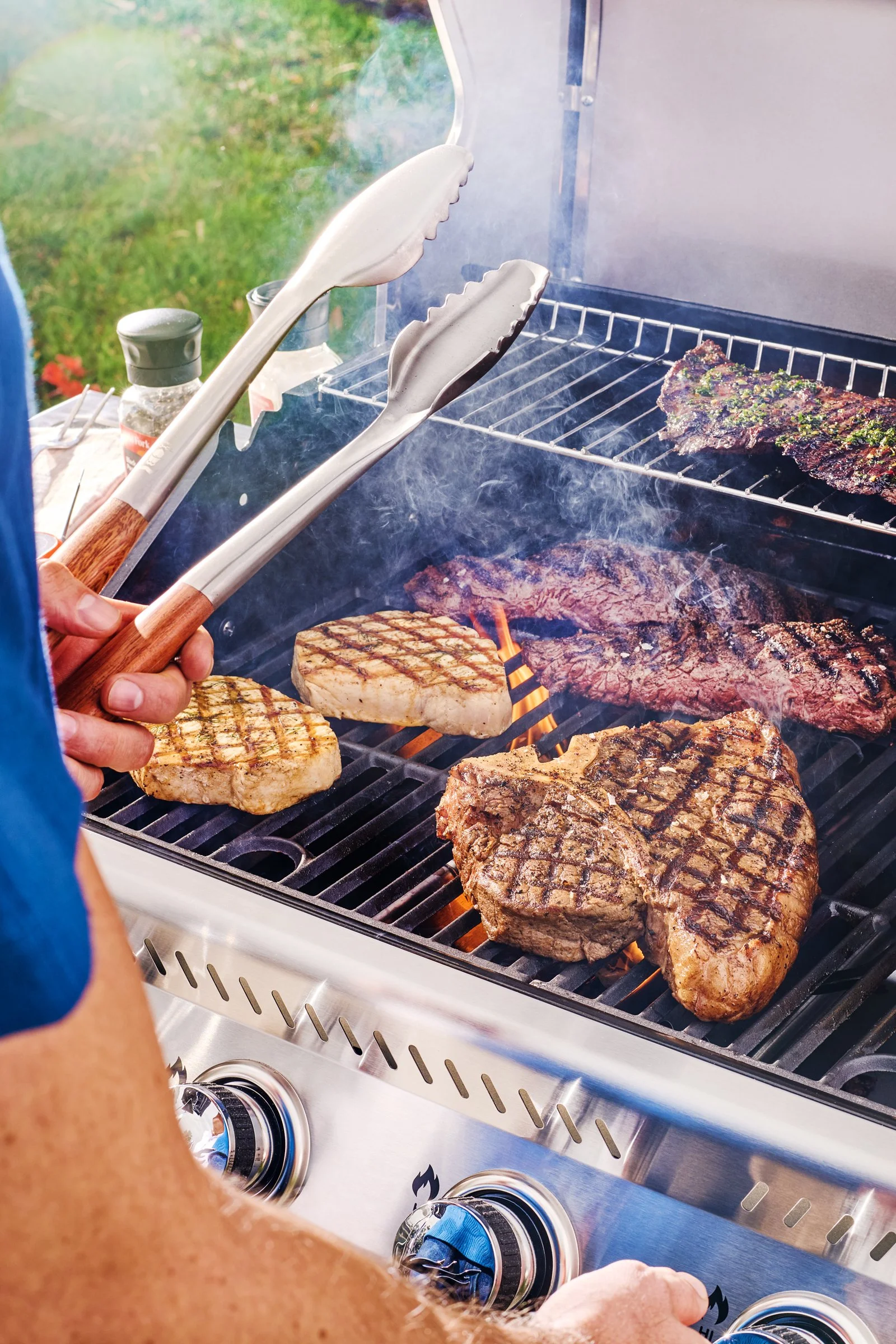 Outdoor lifestyle photography of a man grilling steaks in a backyard setting.