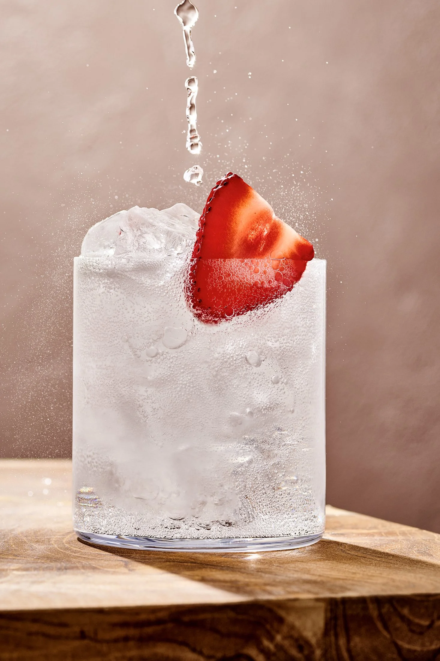Beverage photography of a carbonated drink being poured into glass with fresh strawberry slice. 