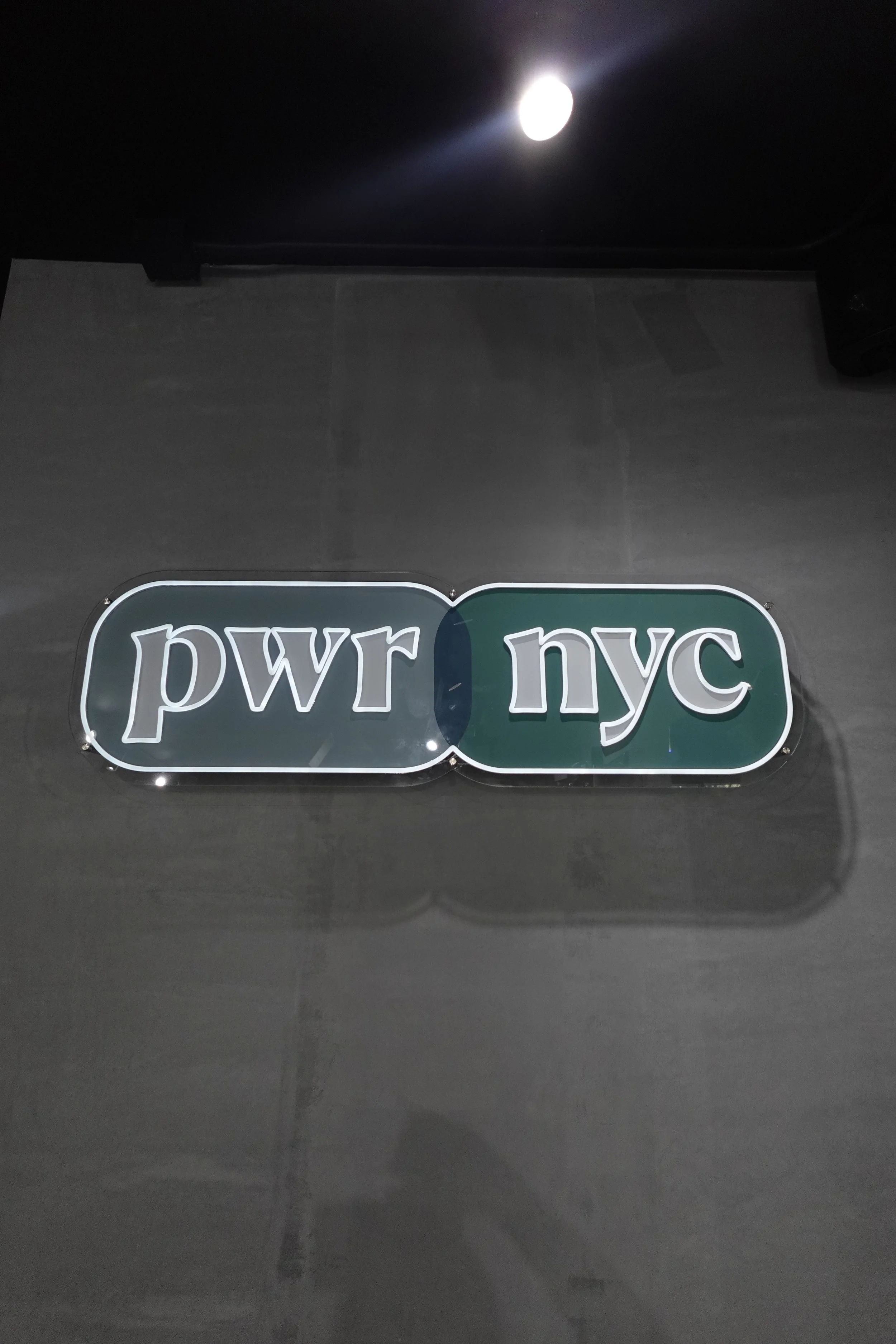 Street sign with the words 'pwr' and 'nyc' on a dark wall.