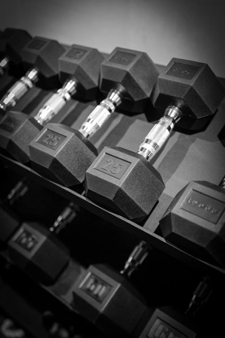 A row of black 25-pound dumbbells on a rack in a gym, black and white photo.