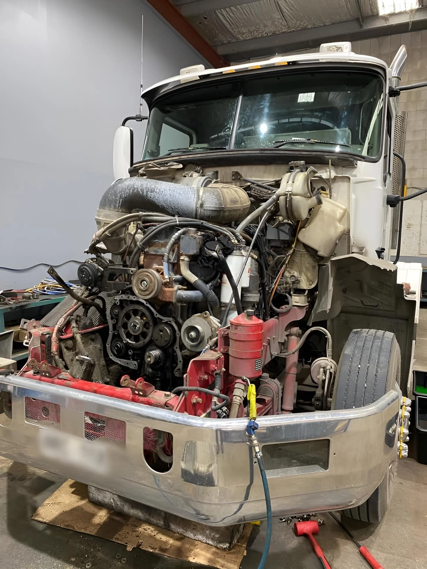 A partially disassembled truck with its front end removed, exposing the engine and various mechanical components inside a workshop.