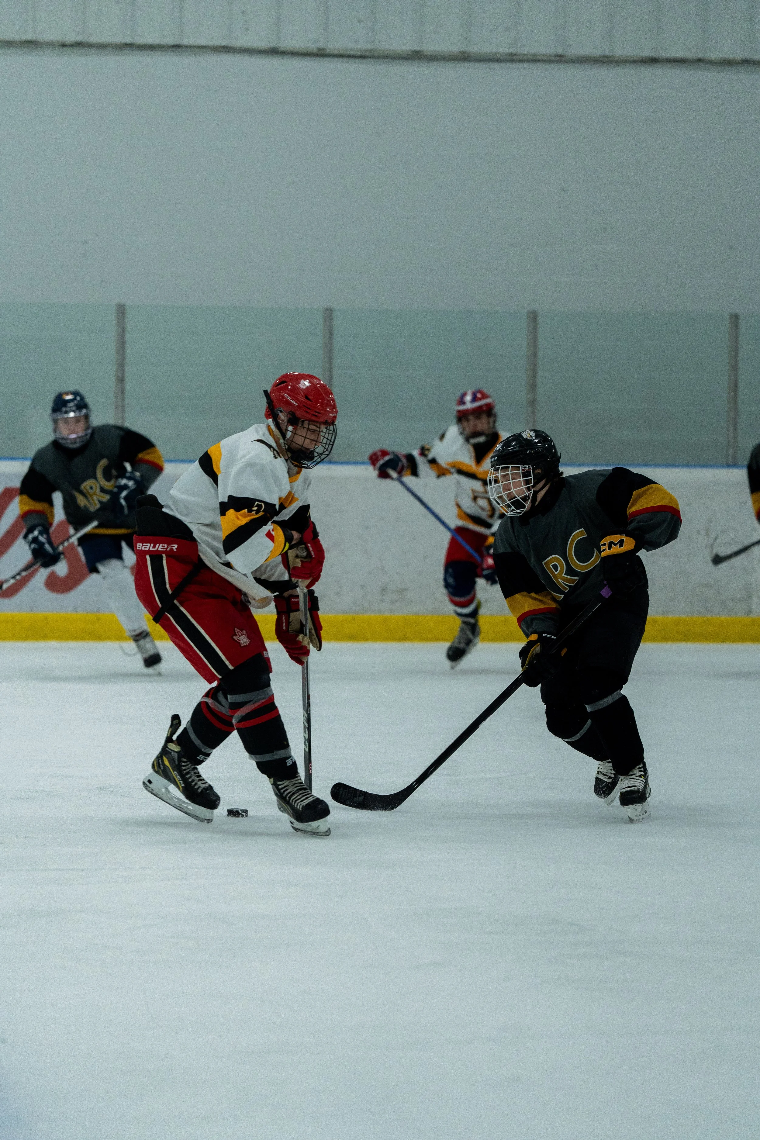 Young hockey players competing on the ice, wearing helmets and jerseys, with two players in focus battling for the puck.