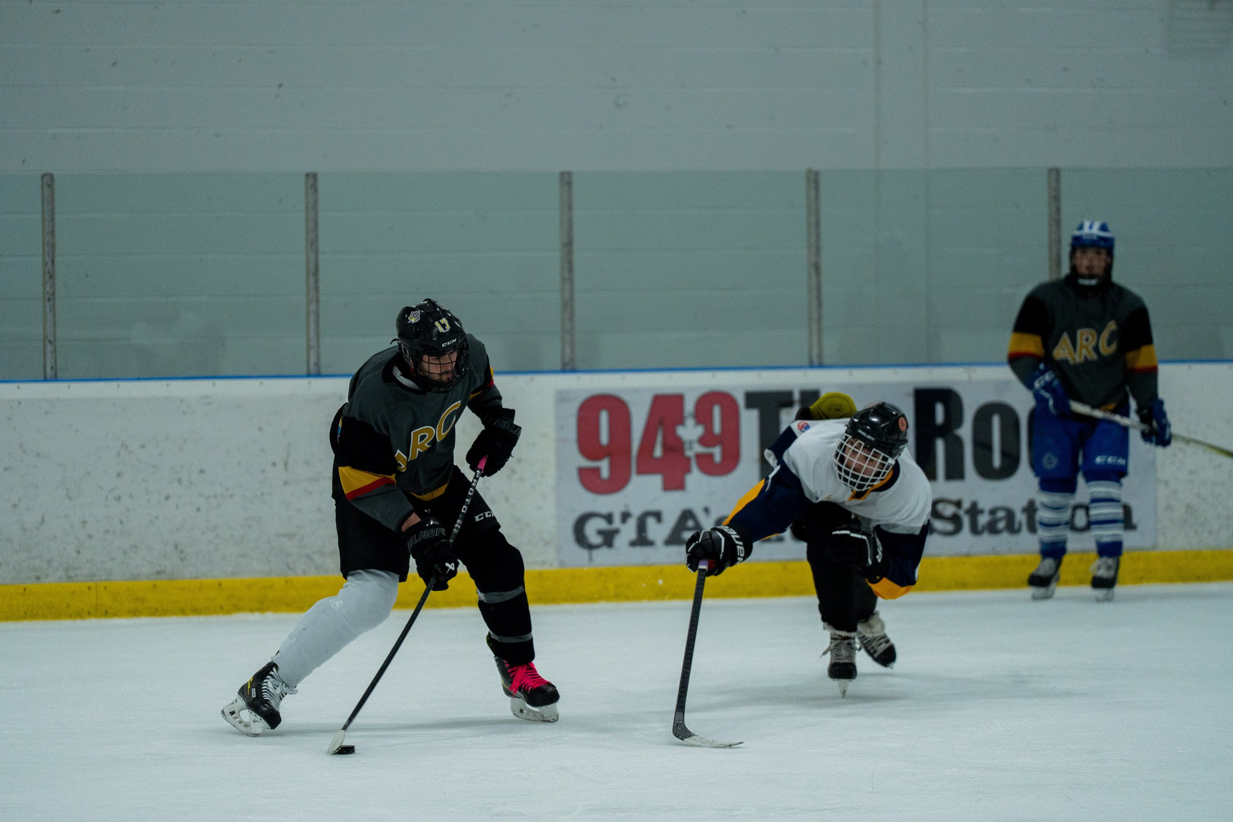 Two hockey players competing for the puck on ice rink, with a third player watching in the background.