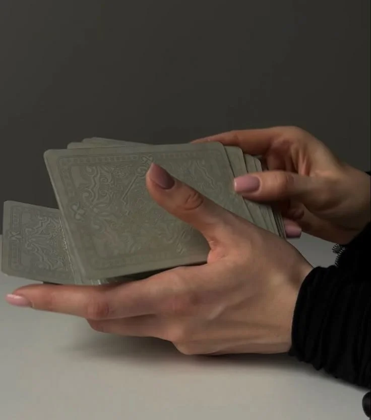 A person holding a stack of playing or tarot cards with a plain background.