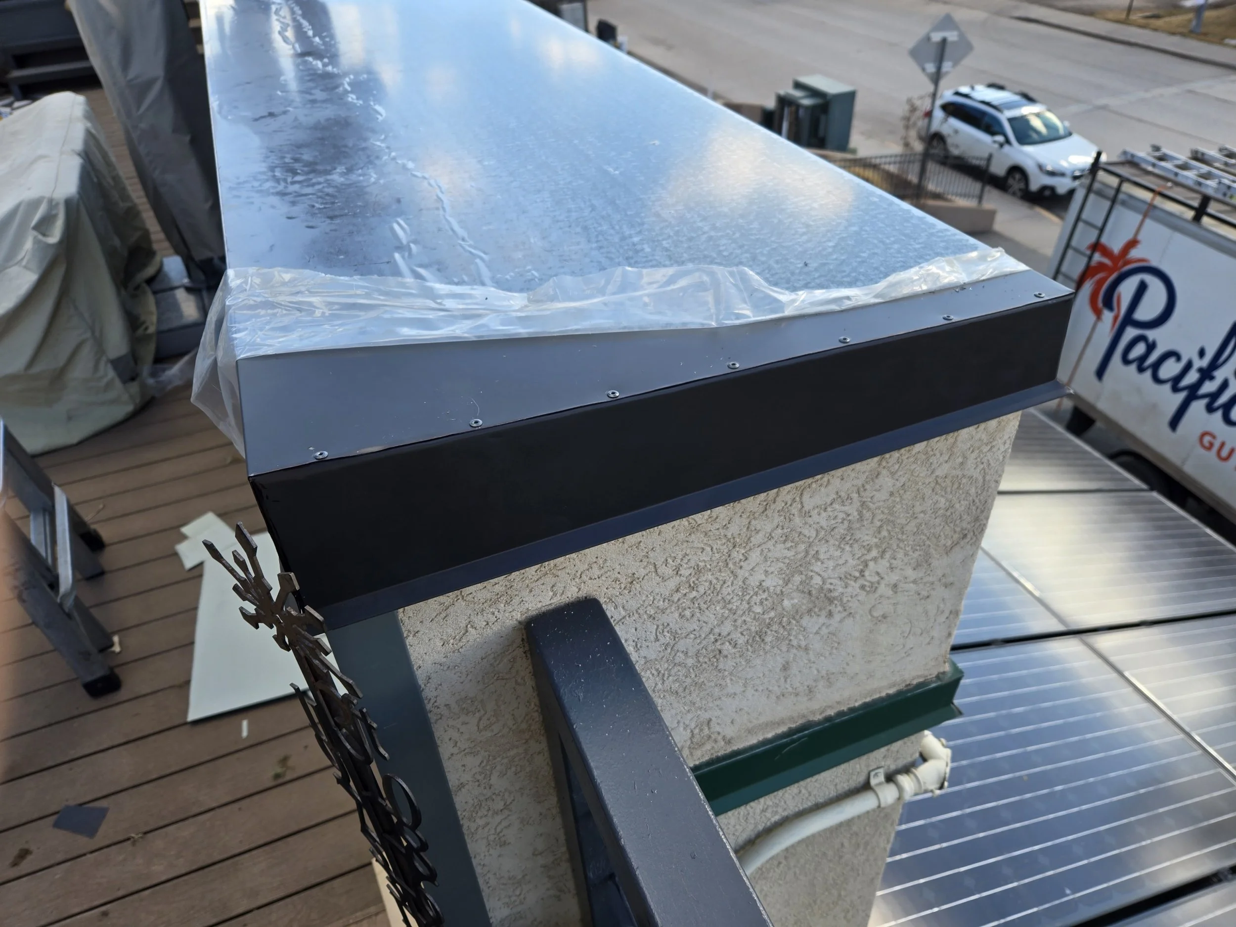 Vista de la parte superior de una chimenea de exterior en un balcón, con la tapa metálica sobre una estructura de concreto y una pipa de ventilación.