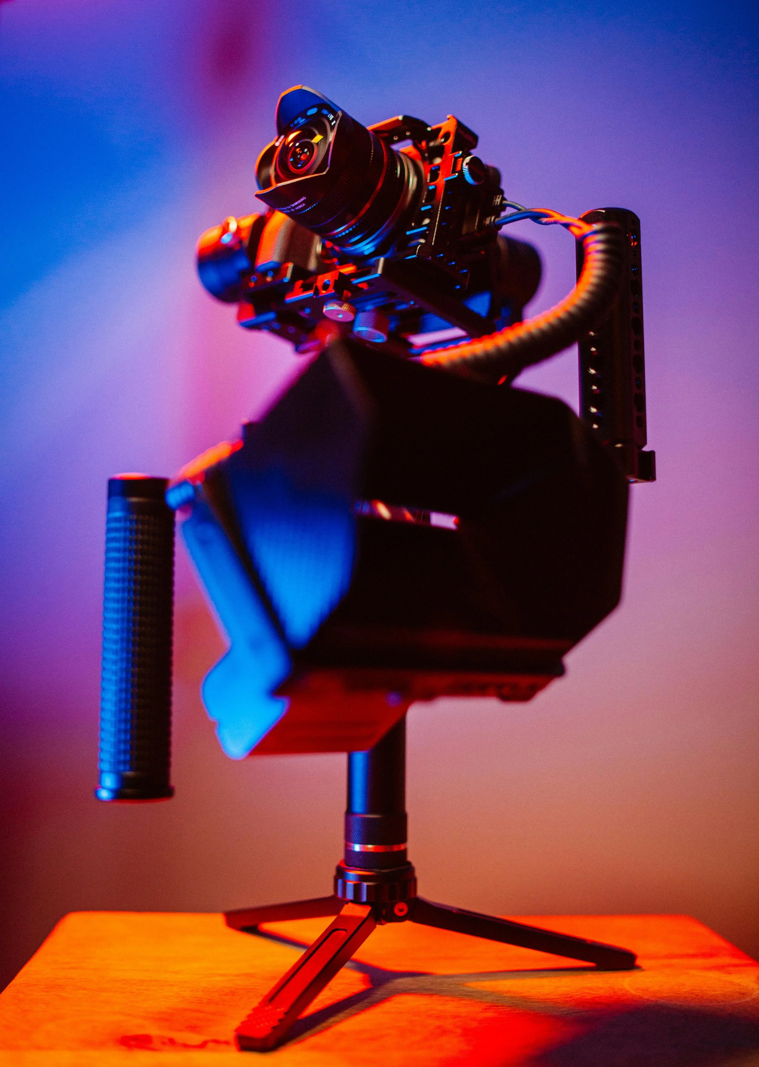 A professional camera mounted on a stabilization rig with colored lighting in the background.