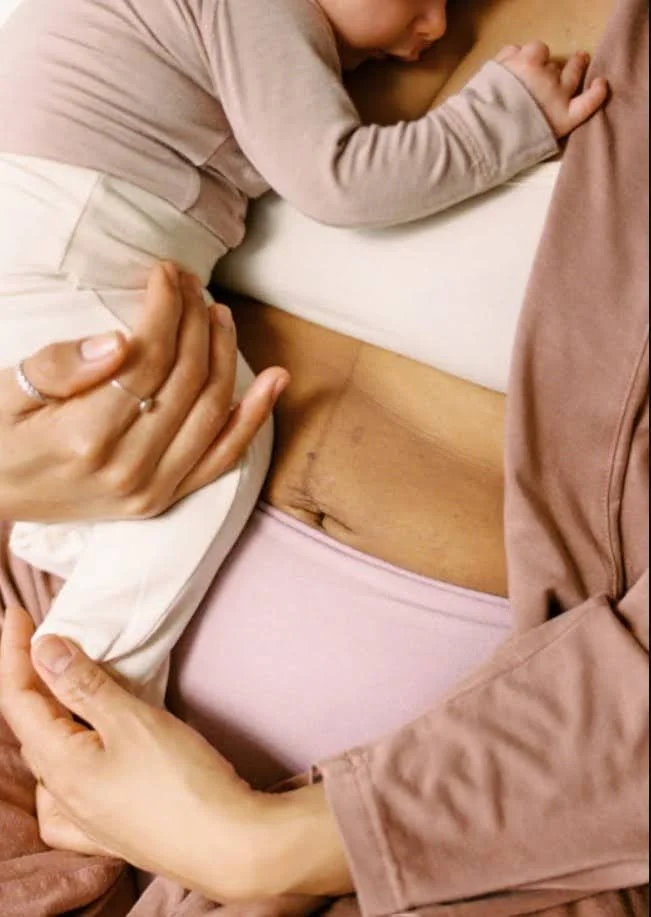 Child leaning on a mother's chest as she holds a baby bump, showing a pregnant belly with hands gently touching its sides.