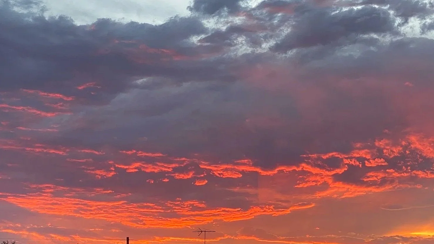 A vibrant sunset sky with gray and pink clouds and an orange glow near the horizon.