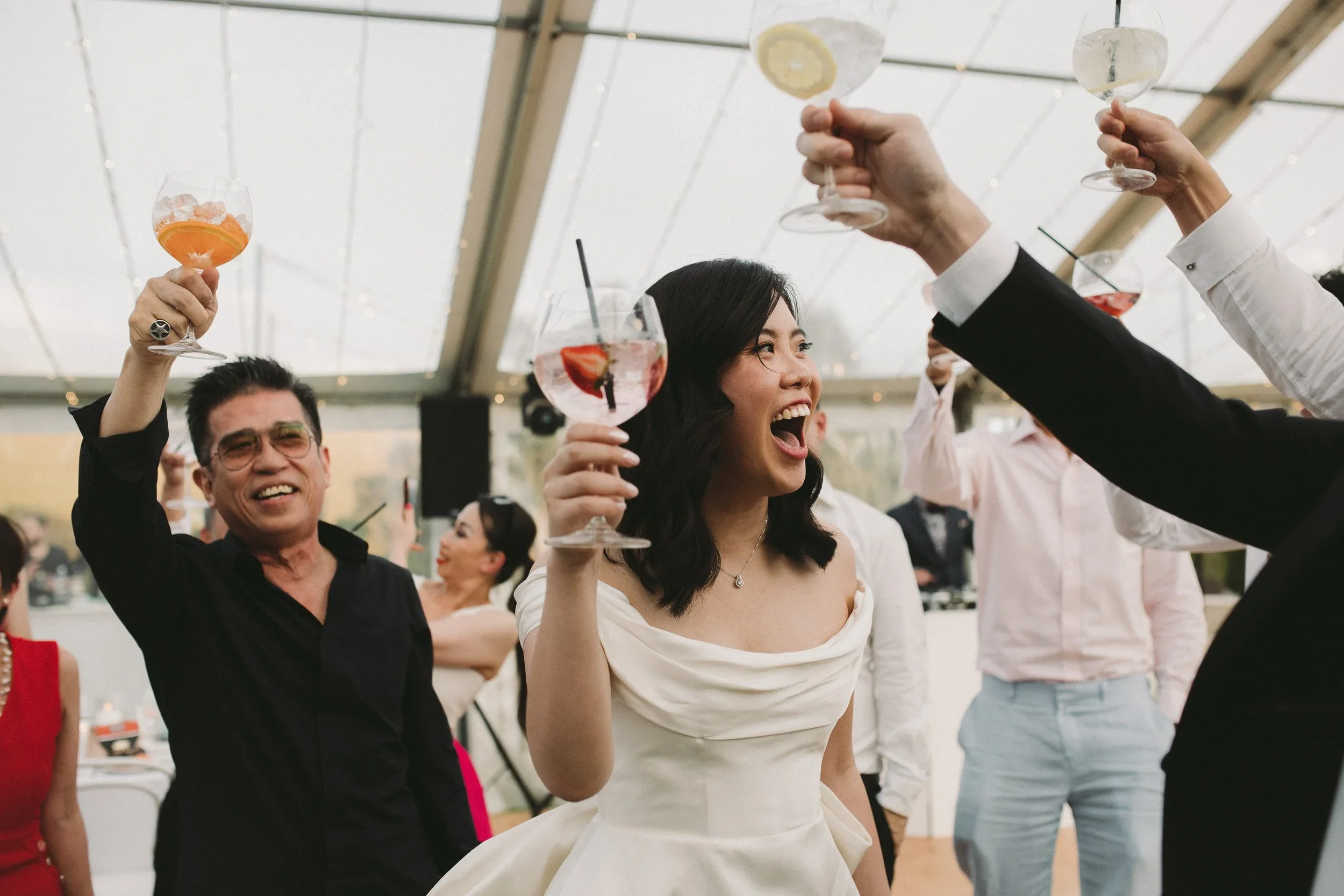 People celebrating with drinks at a festive event indoors, smiling and raising glasses in a toast.