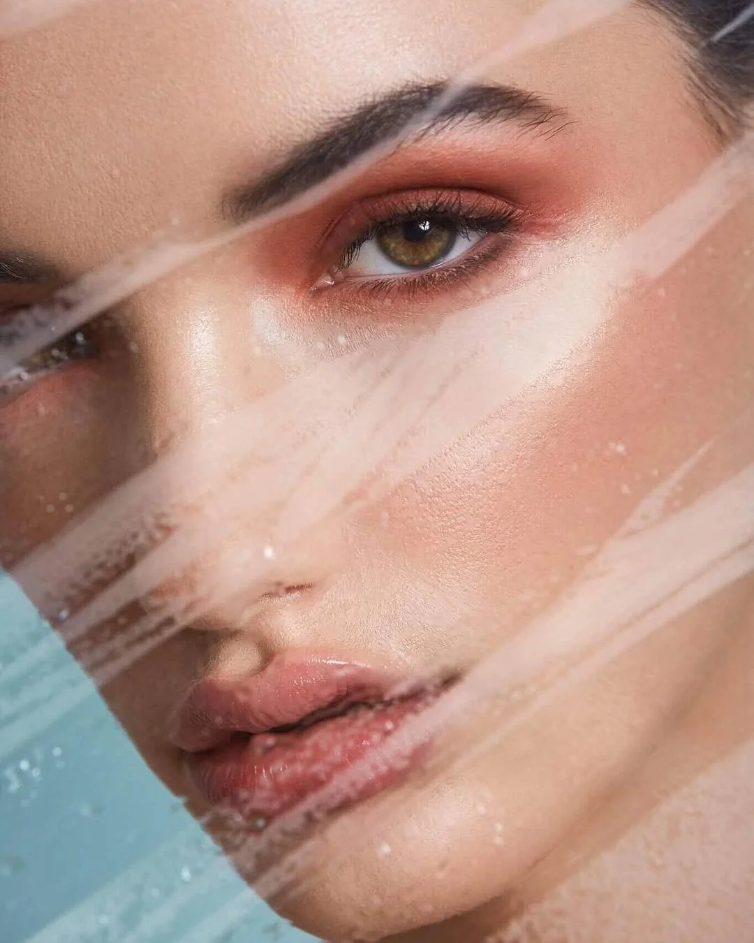 Close-up of a woman's face with water streaks, showcasing her eye, lips, and skin.