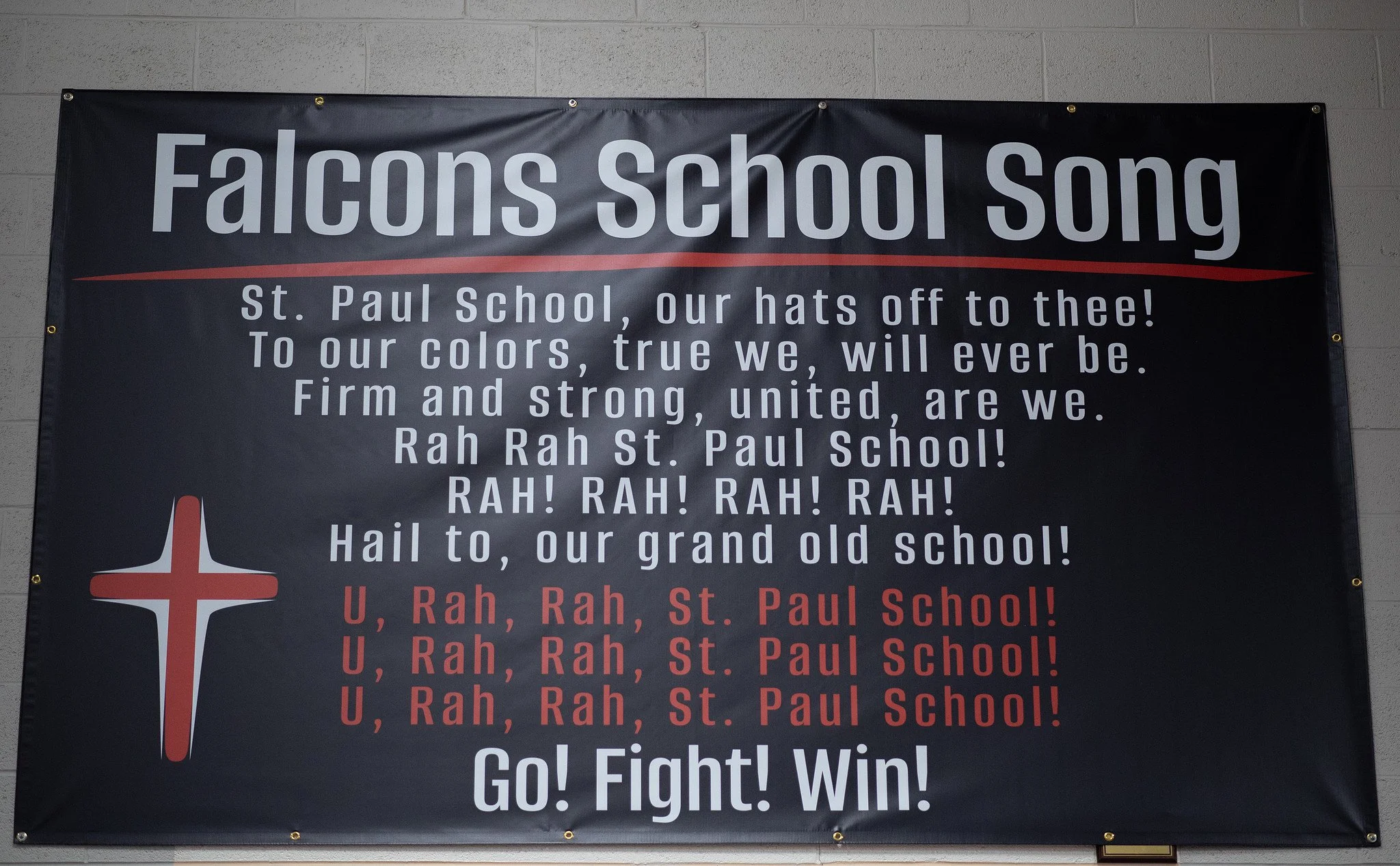A black banner with the title "Falcons School Song" in large white letters at the top, featuring the St. Paul School's cheer with lyrics, a red and white cross on the lower left, and the phrases "U, Rah, Rah, St. Paul School!" and "Go! Fight! Win!" a