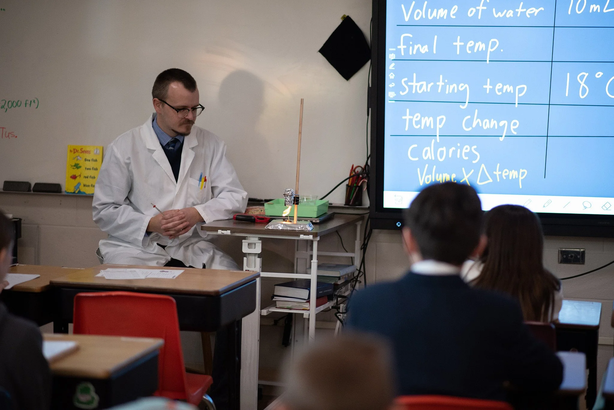 A science teacher demonstrating a small rocket launch with students watching in a classroom.