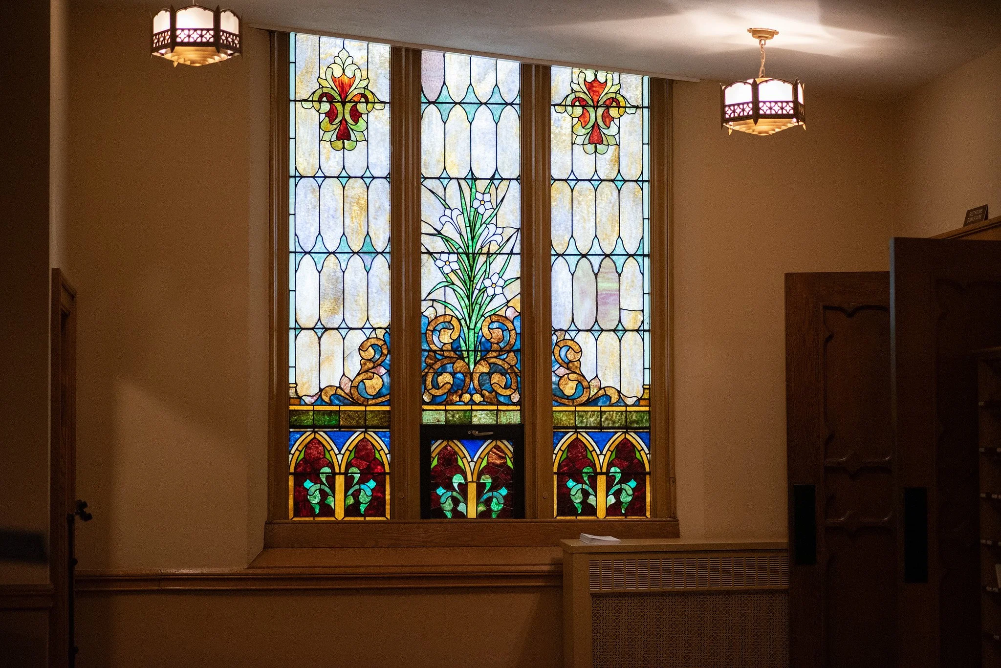 Colorful stained glass window with floral and decorative patterns in a room with beige walls and wooden furniture.