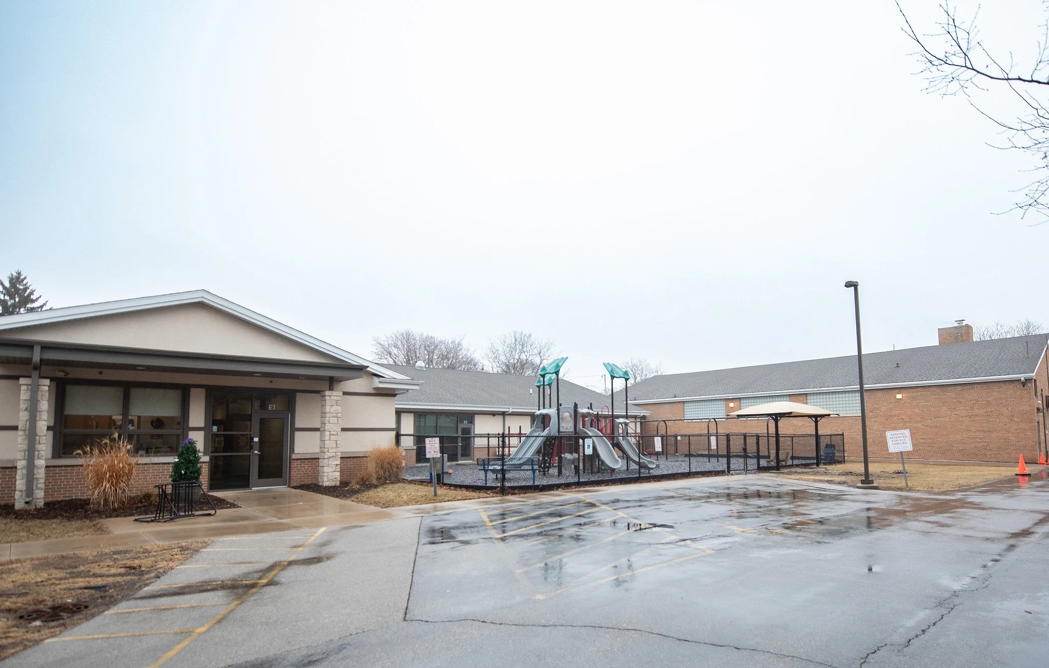 Empty parking lot and a playground with slides in front of a light-colored building on a cloudy day.