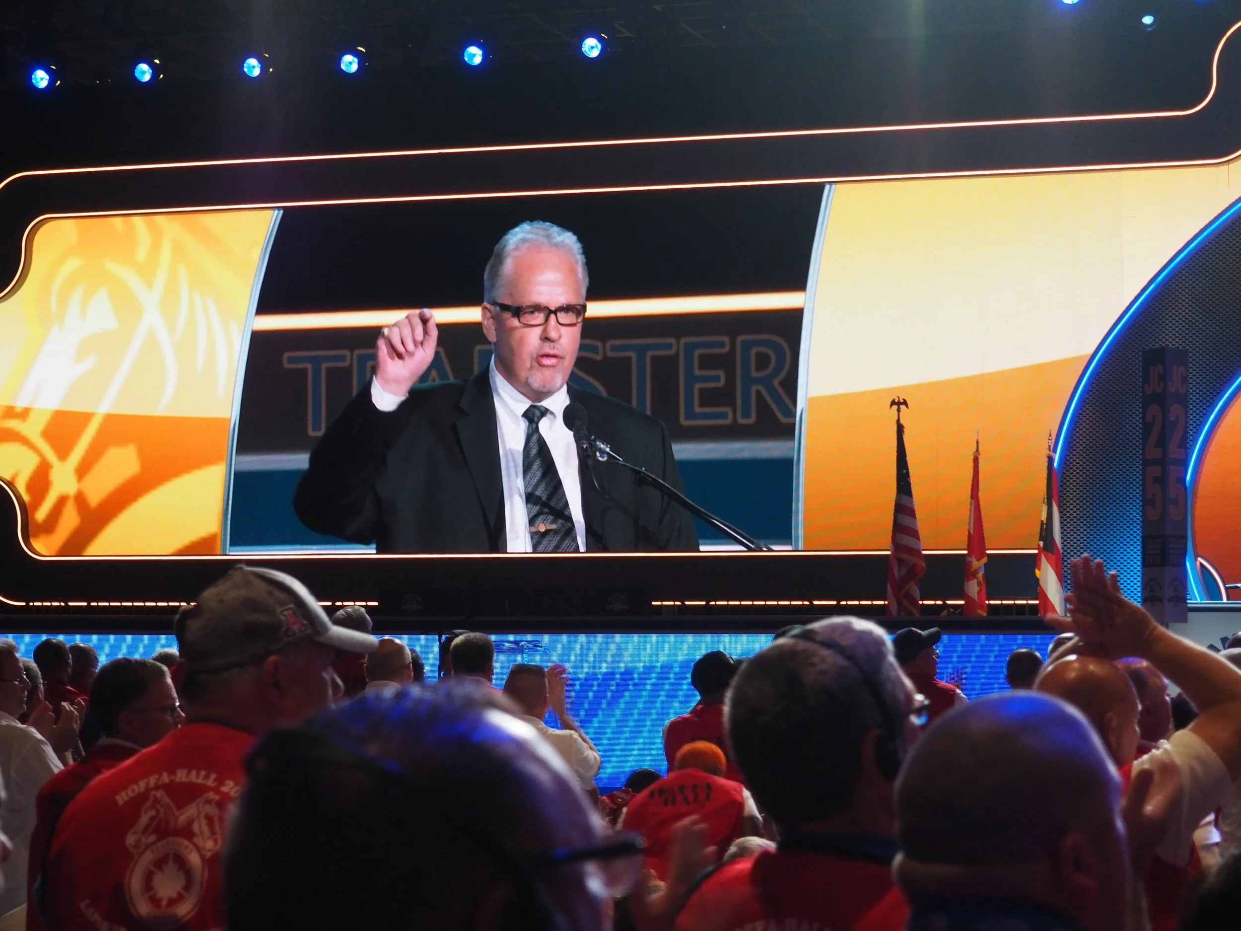 Local 31 President Stan Hennessy speaking to delegates at the Convention, with a large screen behind him displaying his image. The audience stood and clapped for his speech.