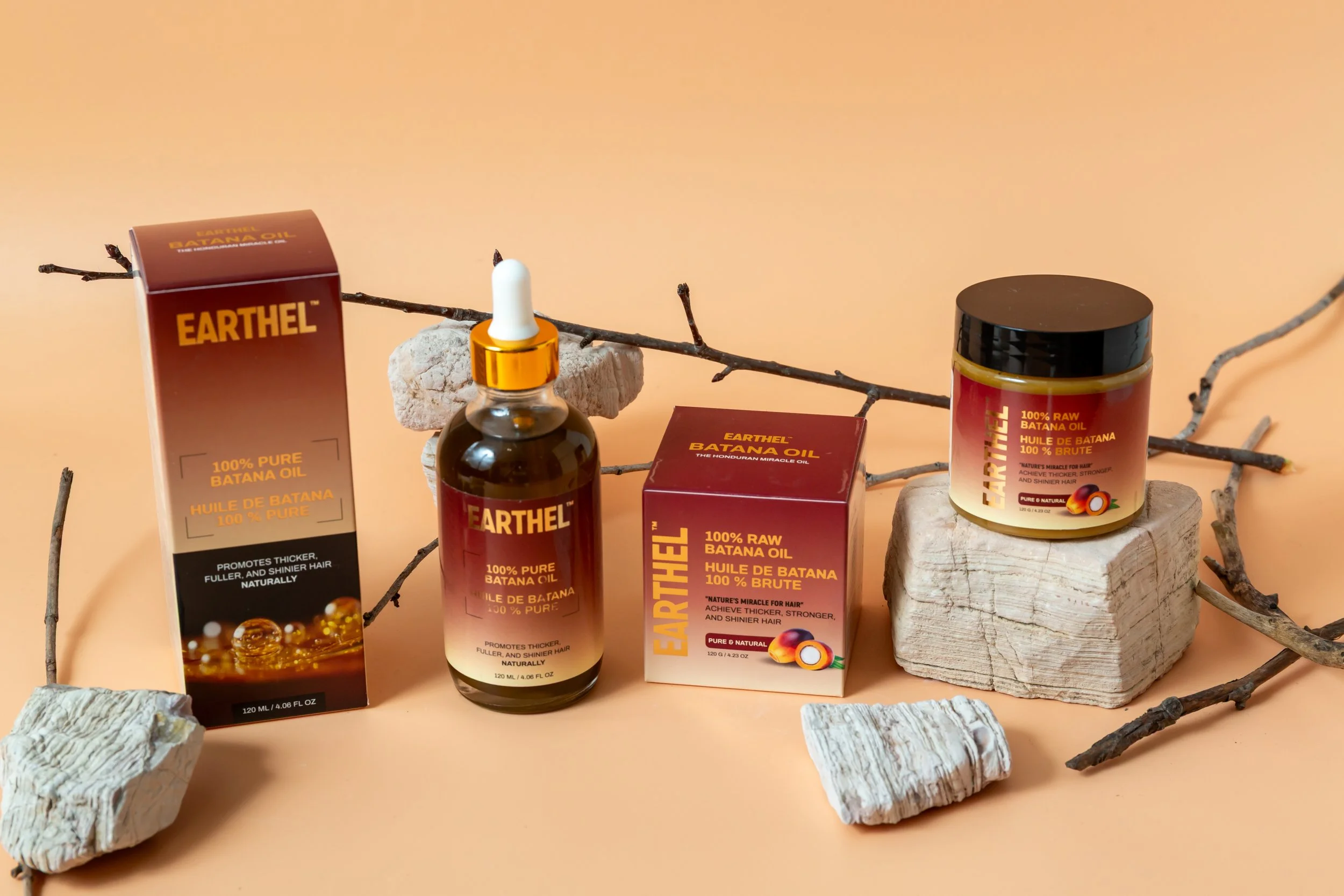 Earthel brand of Batana oil in a box, a bottle with a dropper, and a jar, displayed among rocks and twigs against a beige background.
