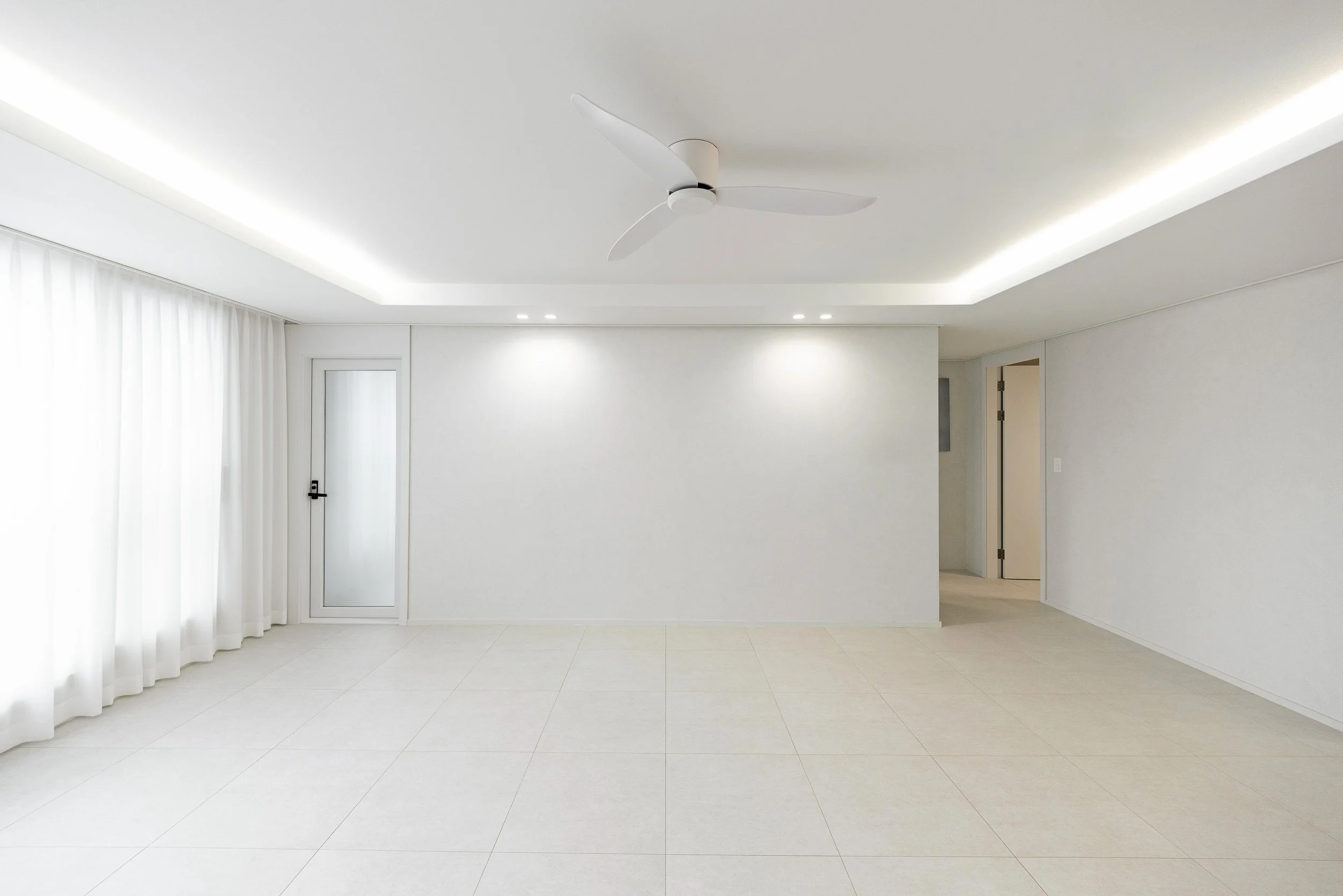 Empty white living room with tiled floor, white curtains, a ceiling fan, and recessed lighting.