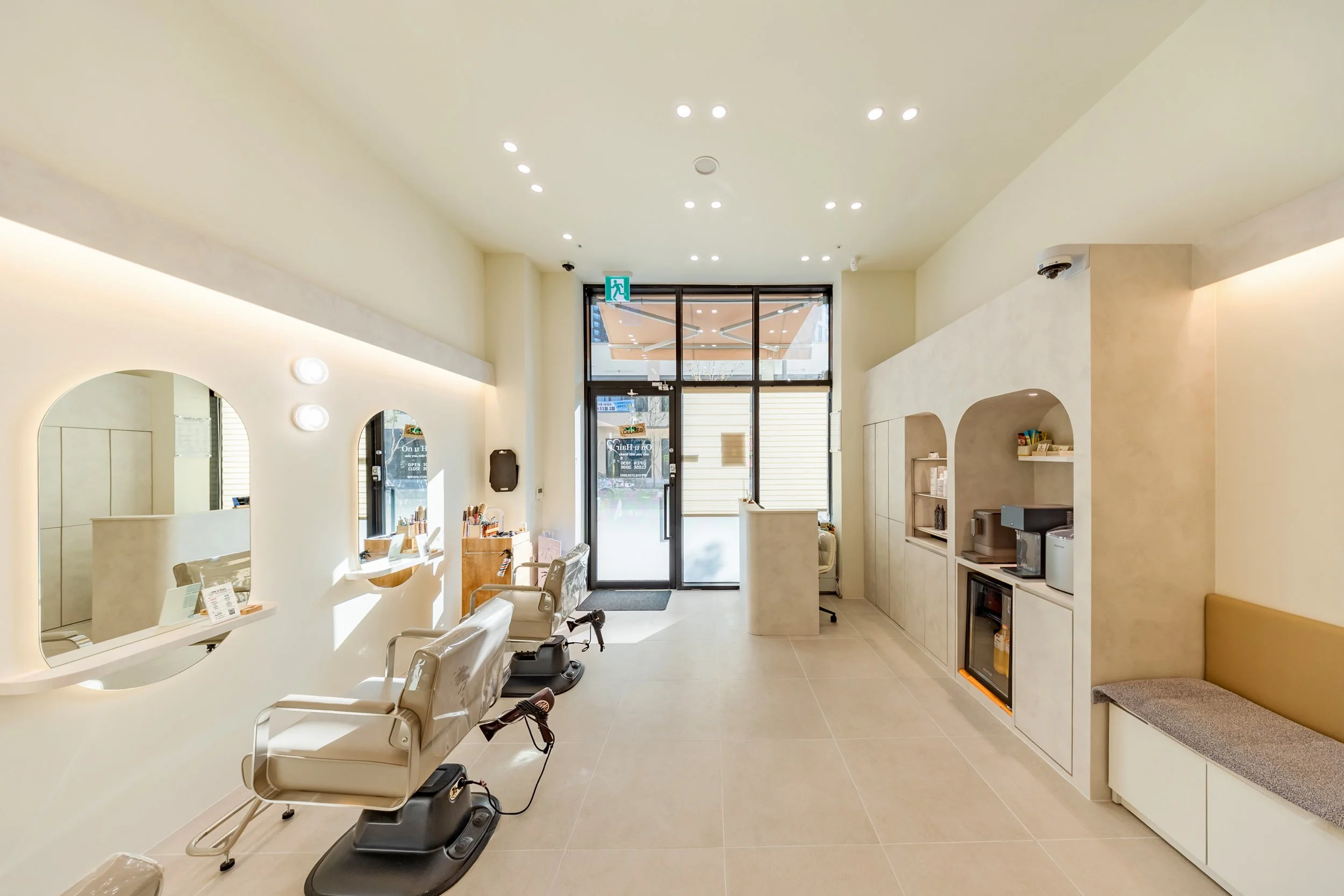 Minimalist haircut salon with white walls, large mirrors, beige chairs, and a glass door entrance.