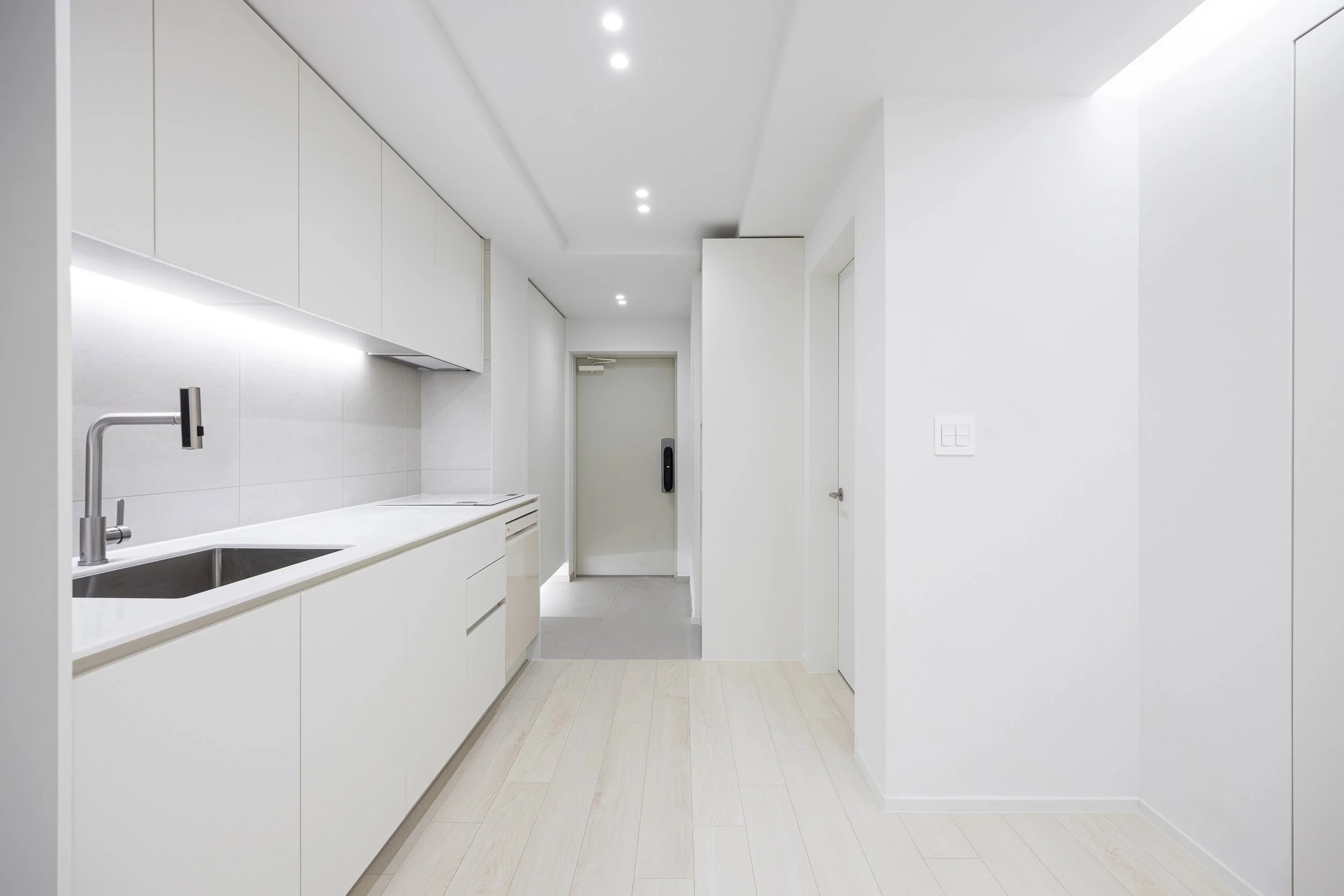 Empty modern white kitchen with built-in cabinets, a sink, and a door leading to an elevator.