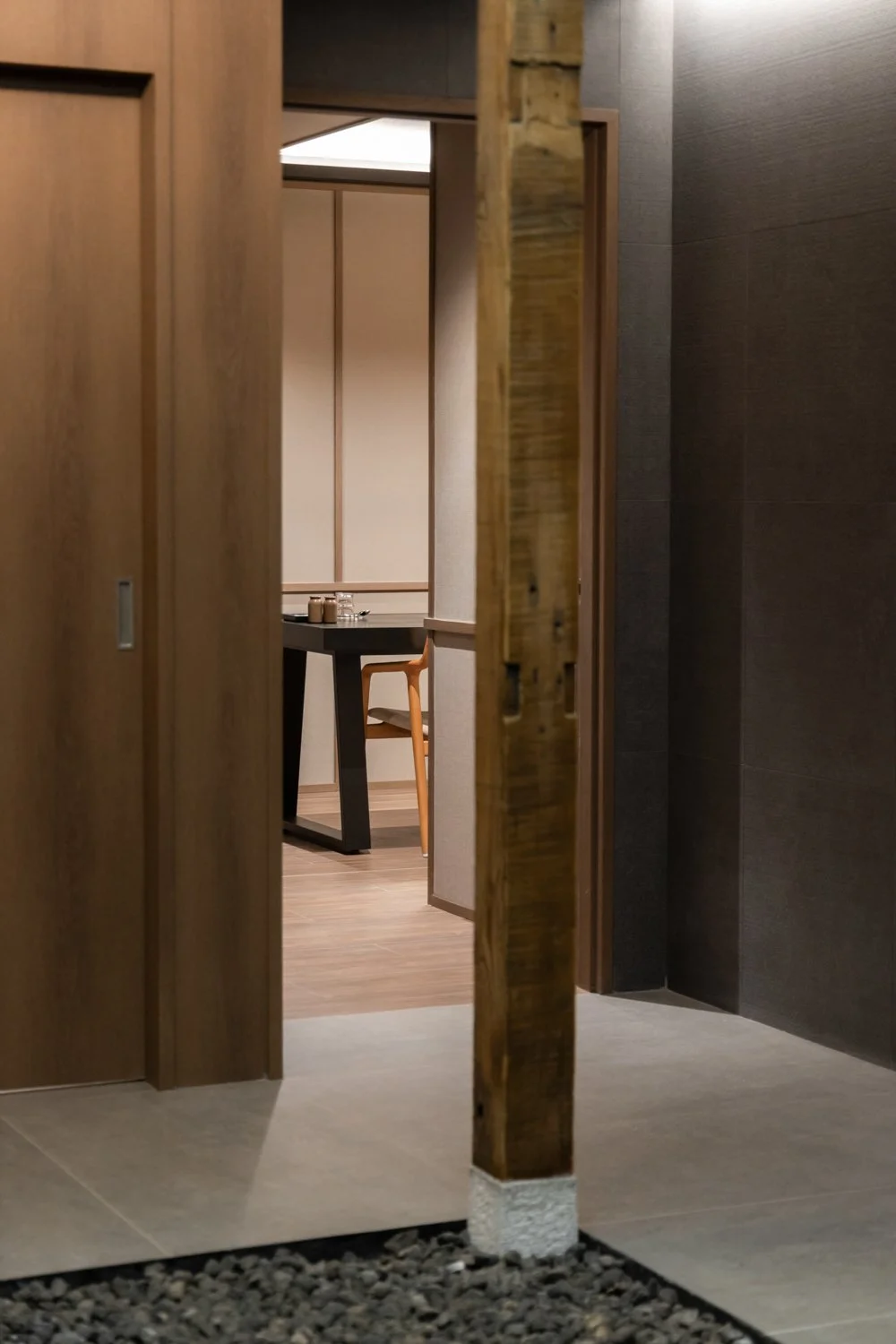 View through a narrow opening into a room with a dark table and wooden chair, modern interior design with wood and dark-colored walls