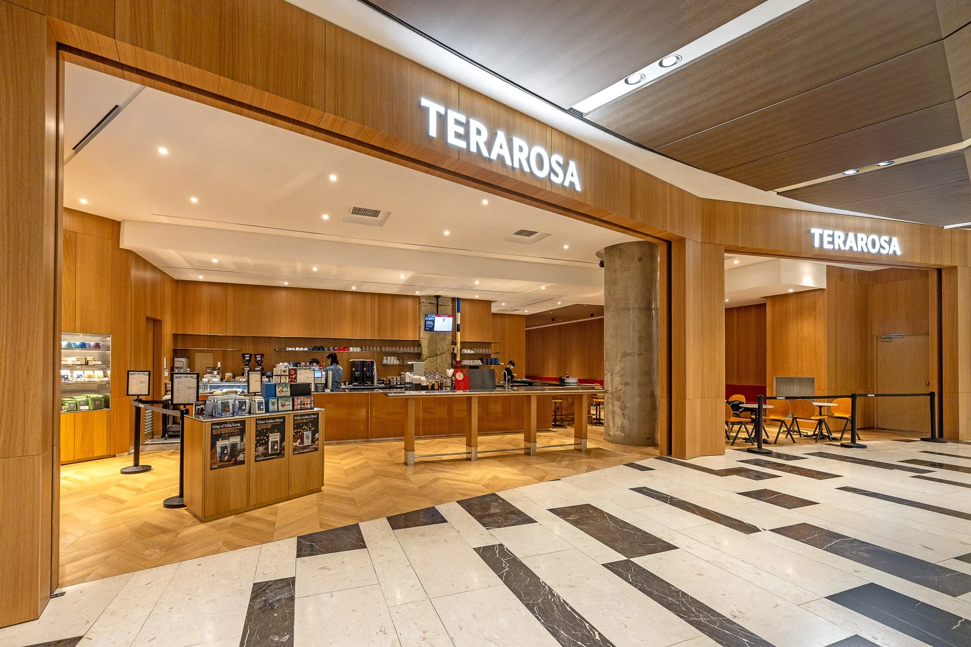 Interior view of Terarosa coffee shop with wooden decor, counter, coffee machines, and seating area in a shopping mall.
