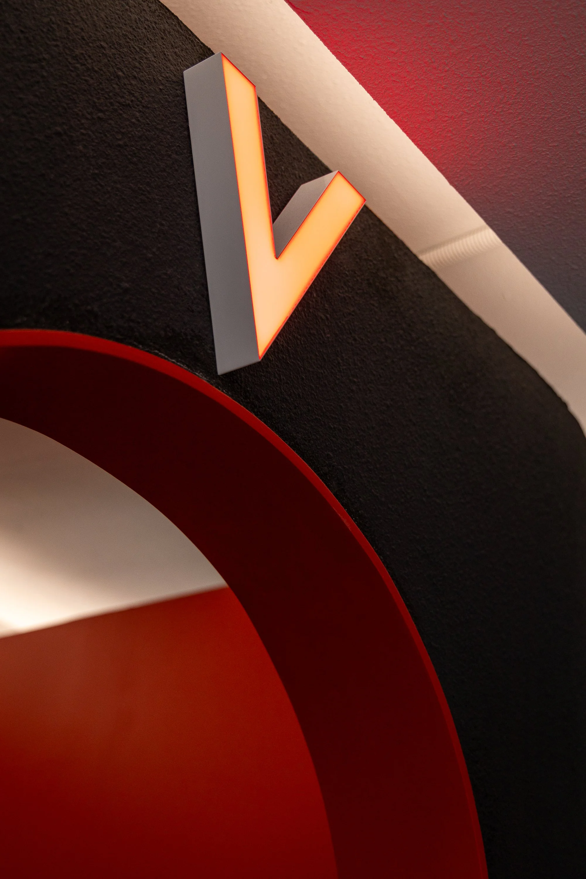 Close-up of a red and white illuminated arrow sign on a textured black wall in an interior setting.