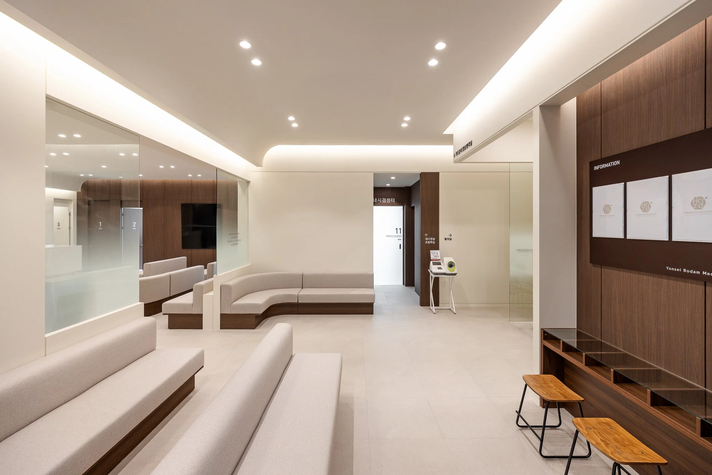 Empty modern waiting room with beige couches, wooden accents, and a large wall-mounted TV.