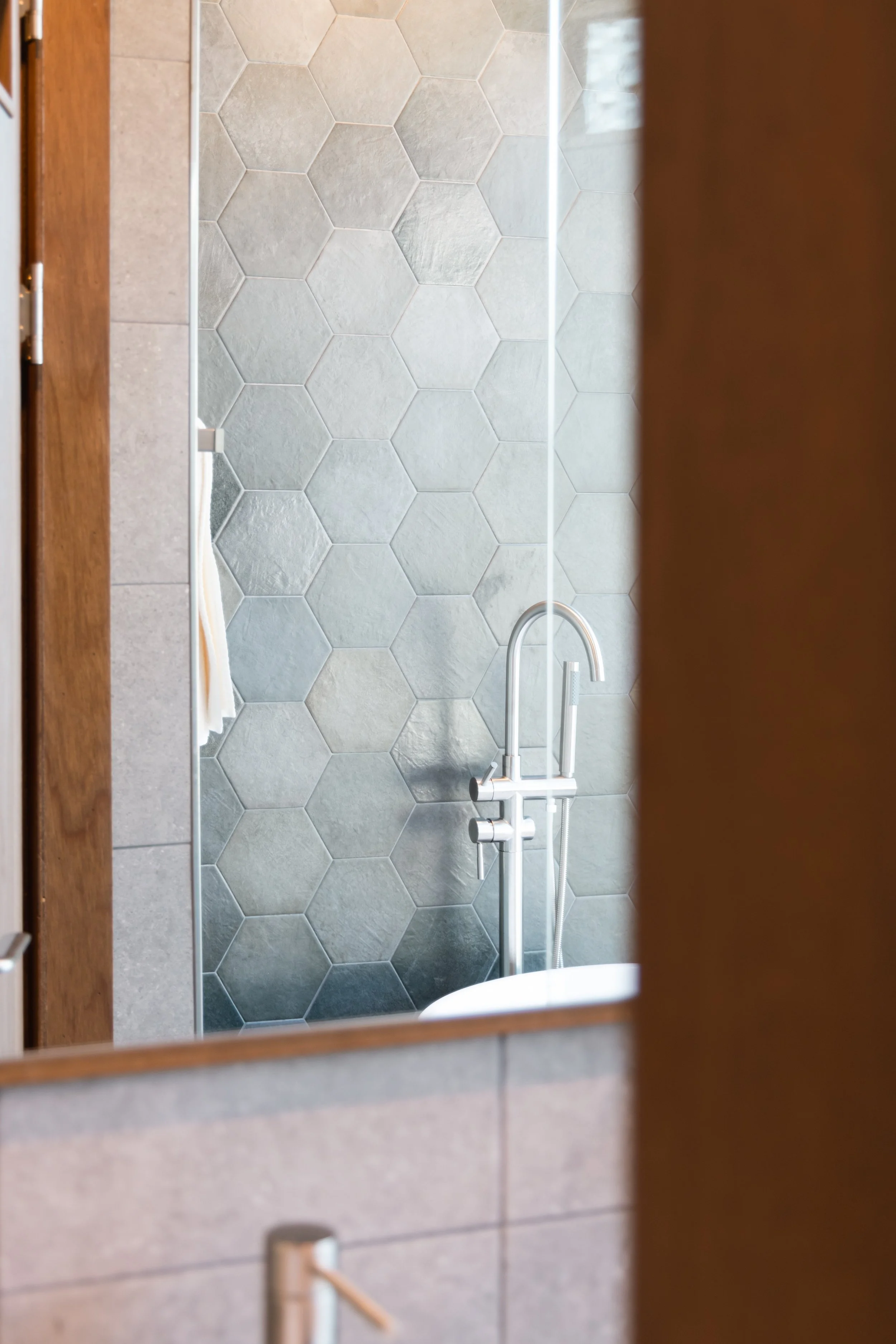 Bathroom shower area with hexagonal tiles, a silver showerhead, and a partial view of a towel.