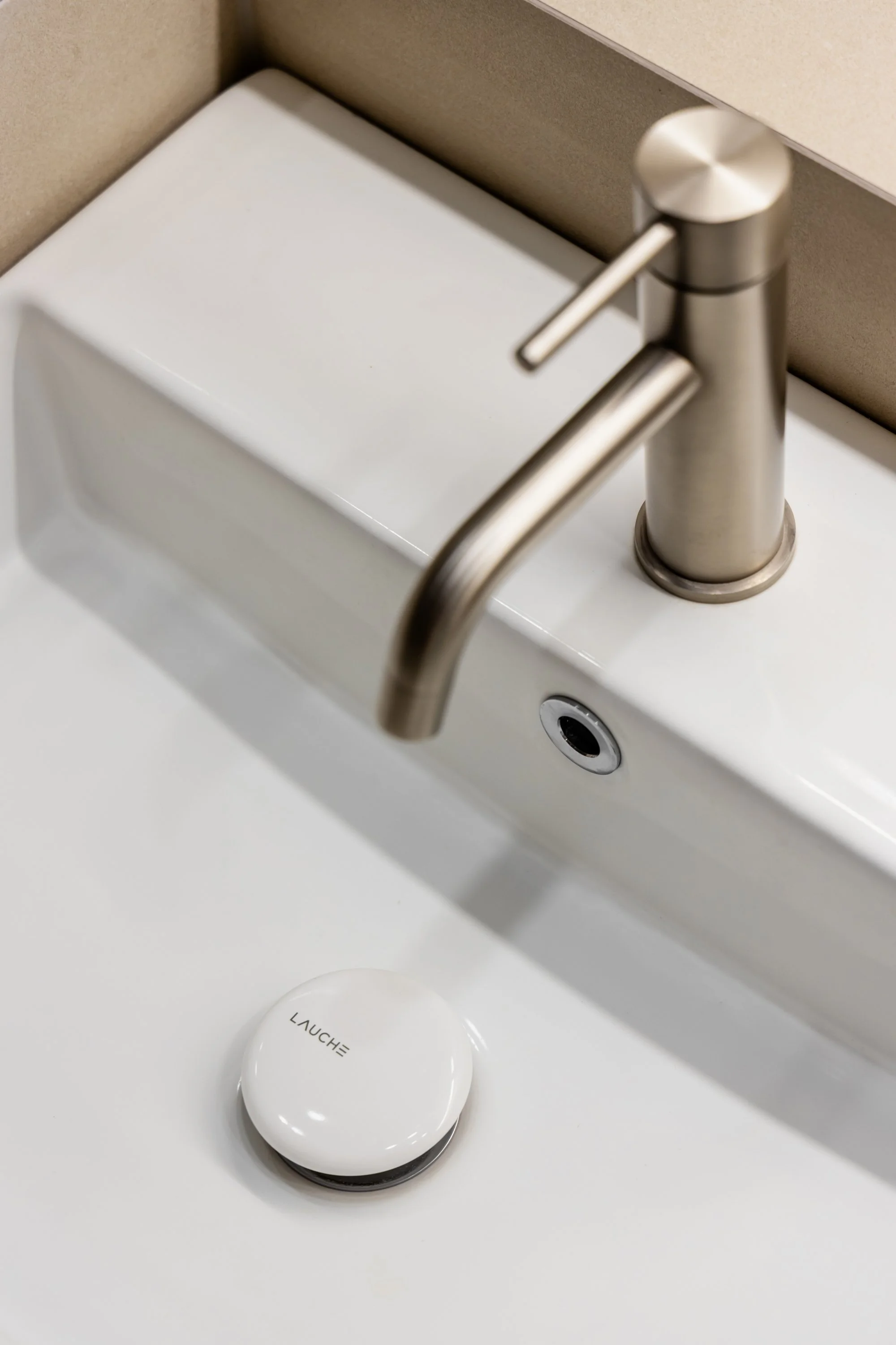 Close-up of a modern bathroom sink with a brushed metal faucet, a white soap dish, and a round device labeled 'LAUCH' on the countertop.