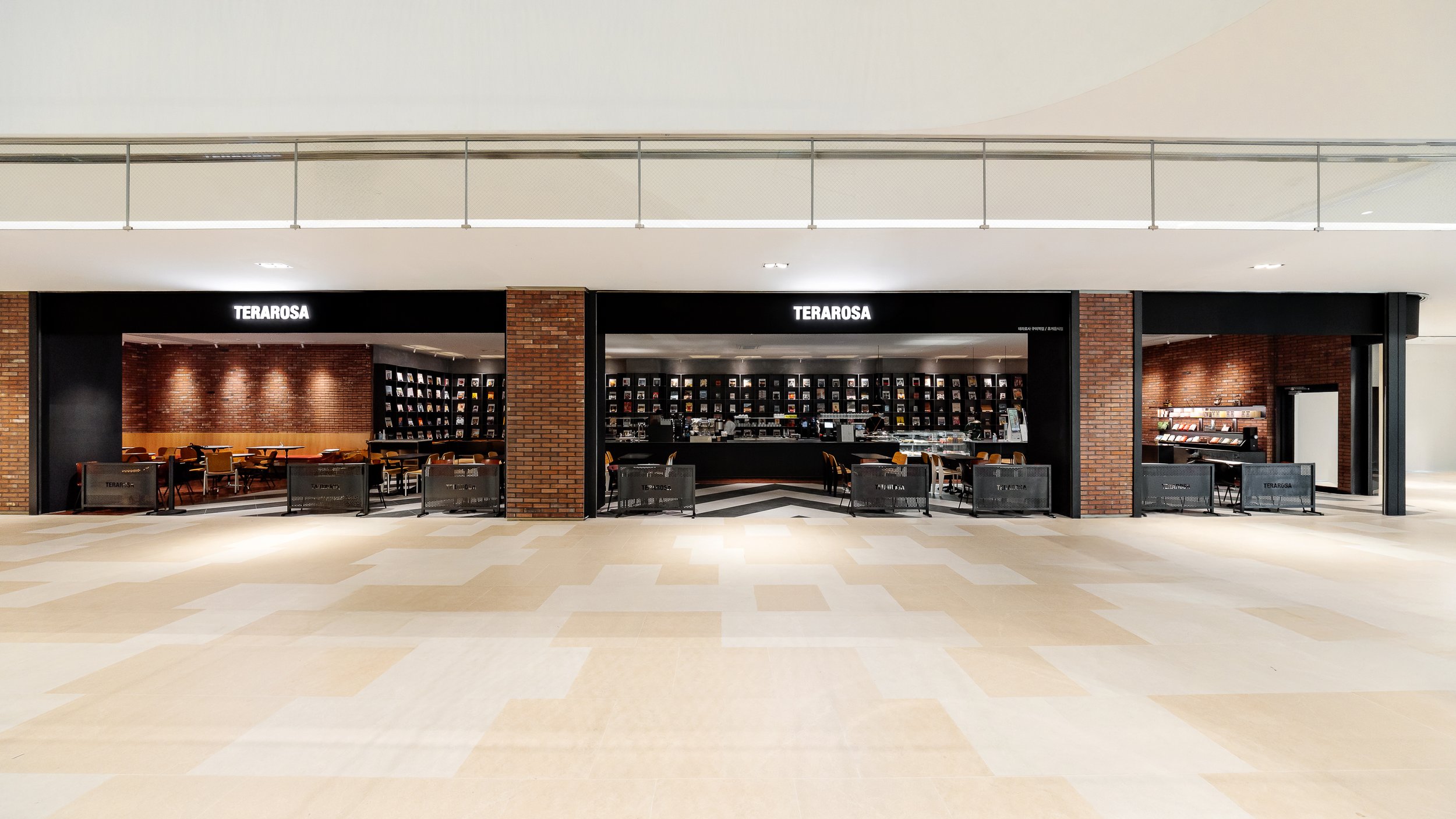 Exterior view of a dark-colored cafe called 'TERAROSA' with seating outside, large windows, and brick walls inside.