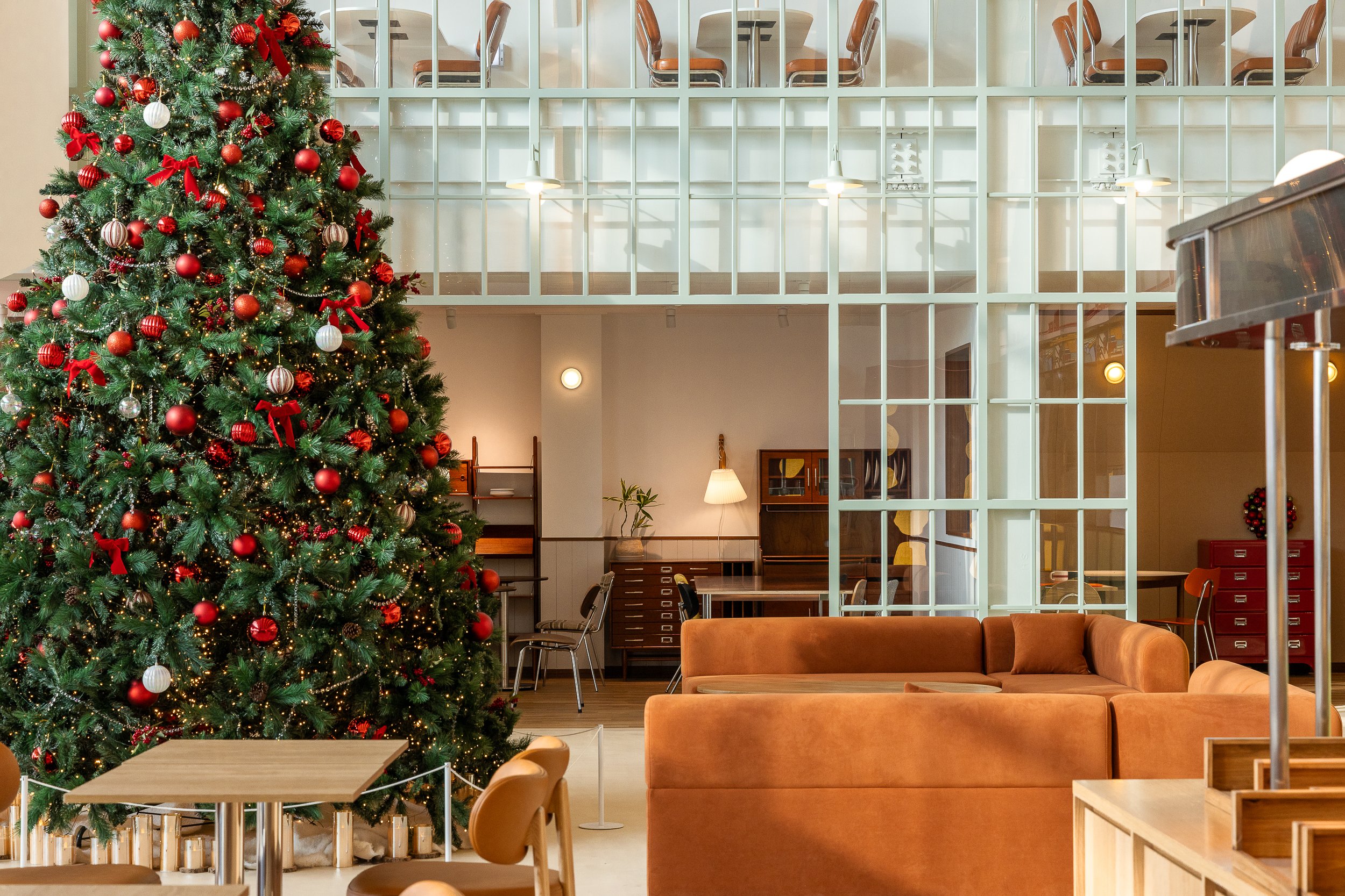Decorated Christmas tree inside a modern, cozy lobby area with seating and wooden furniture.